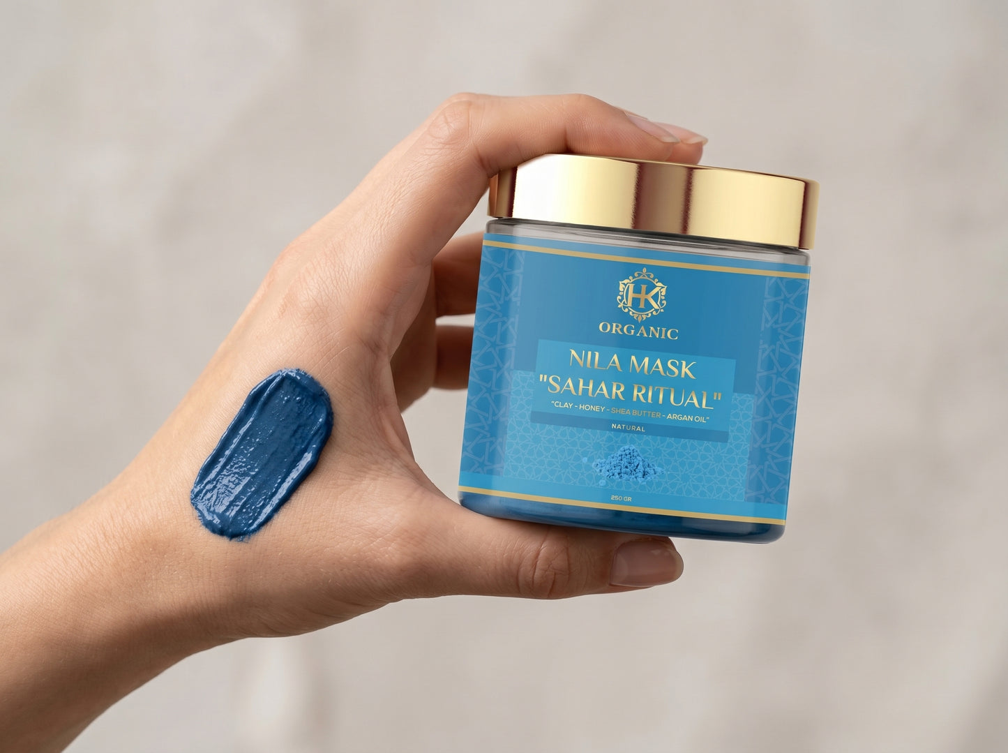 Hand holding a blue skincare product container with gold lid against a neutral background