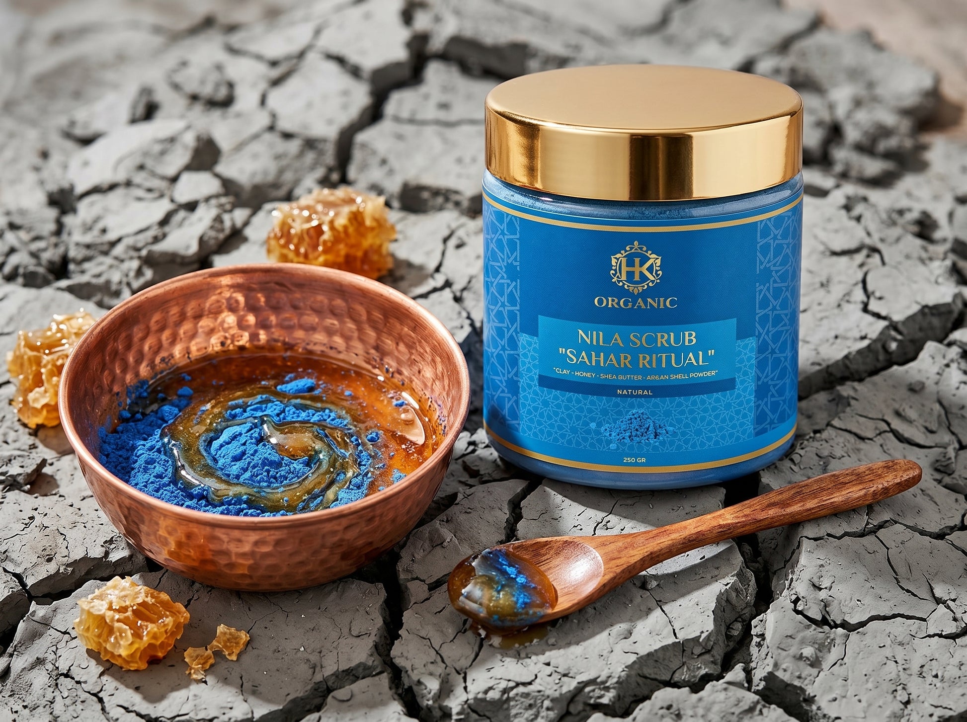 Blue scrub jar with gold lid on a cracked surface, surrounded by a bowl of blue powder and a wooden spoon.