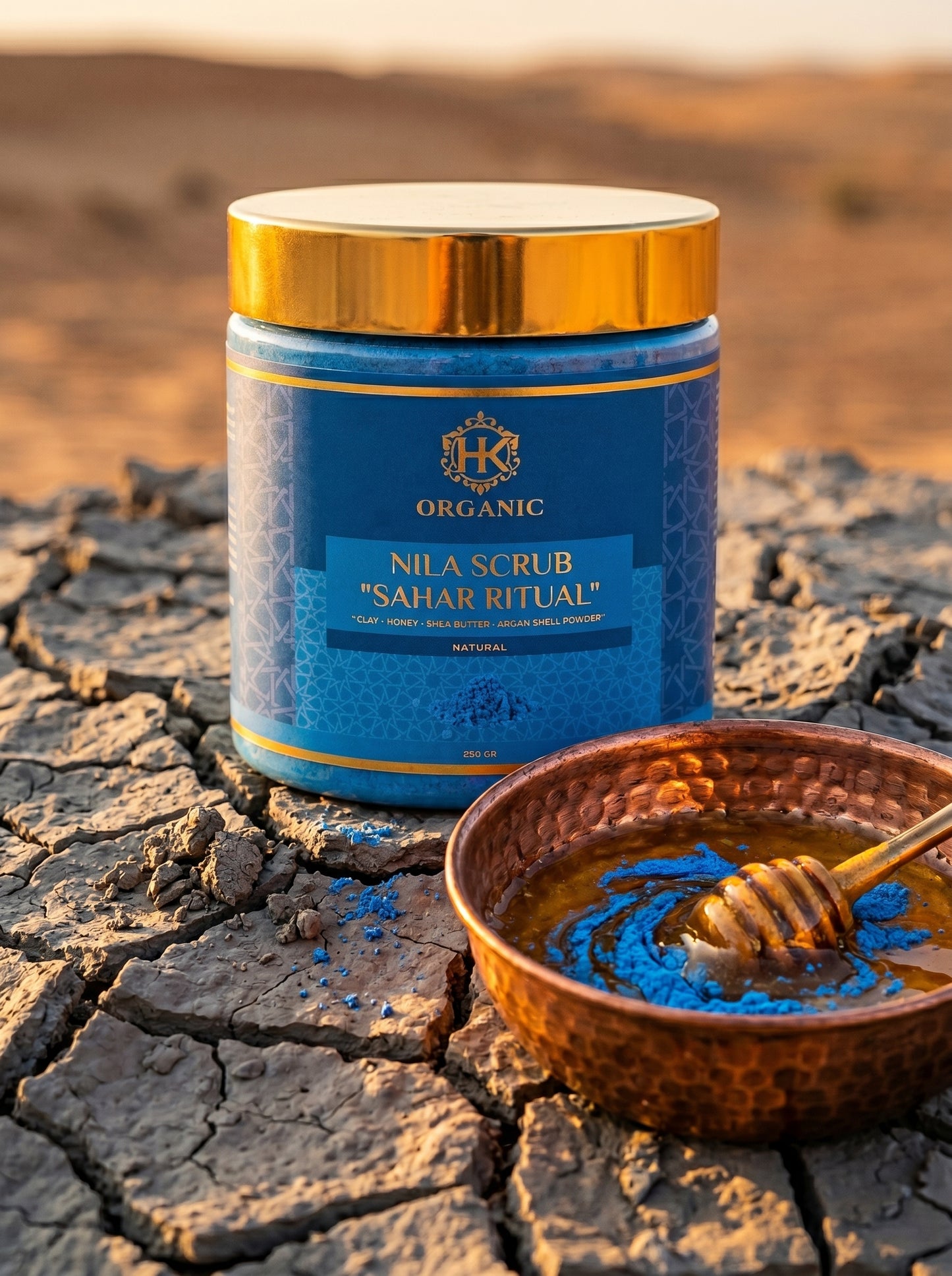 Blue jar labeled 'Nila Scrub Sahar Ritual' on a desert background with a bowl of blue powder and honey.