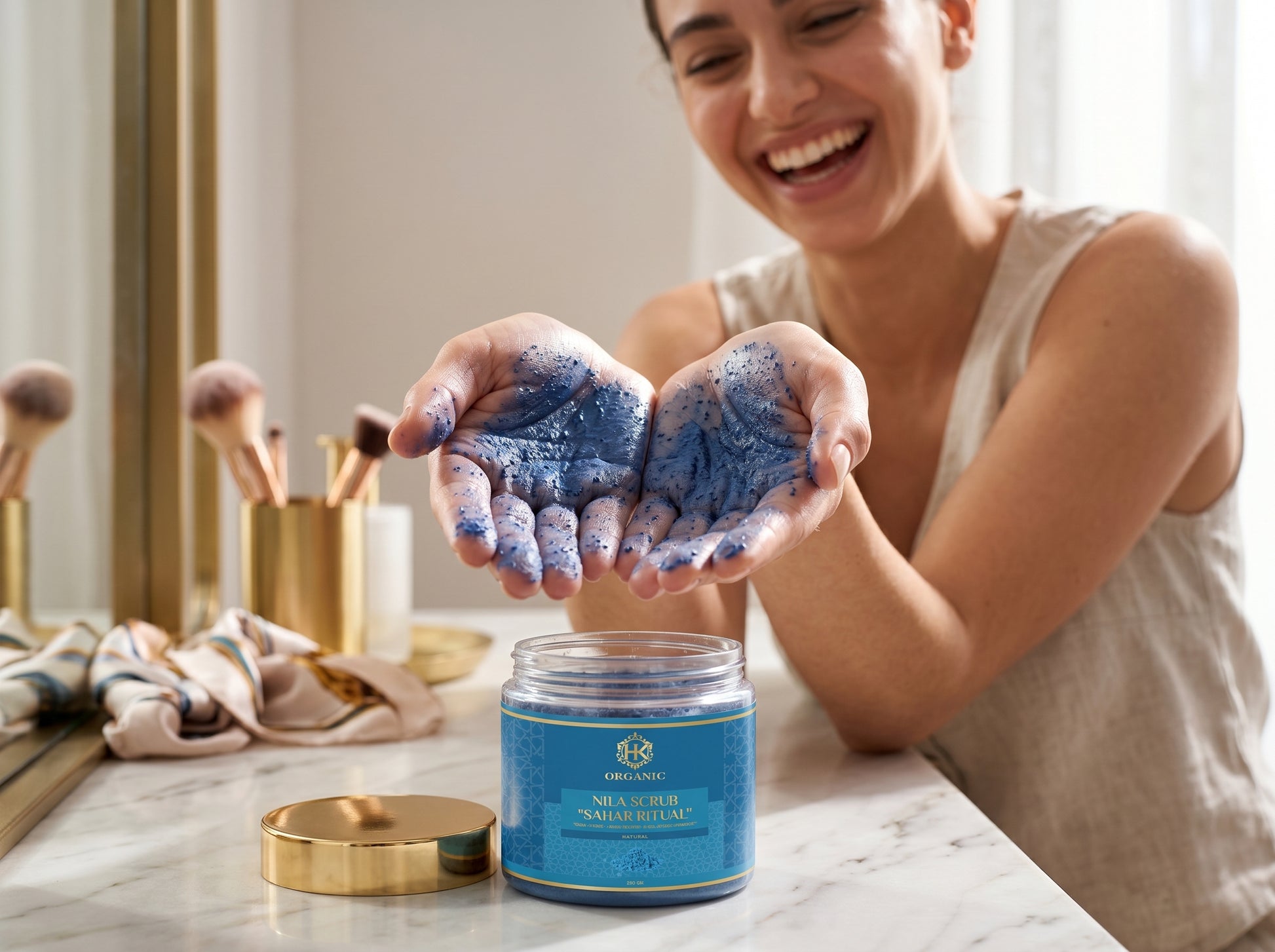Woman holding blue exfoliating scrub in hands with a jar of the product on a marble surface.