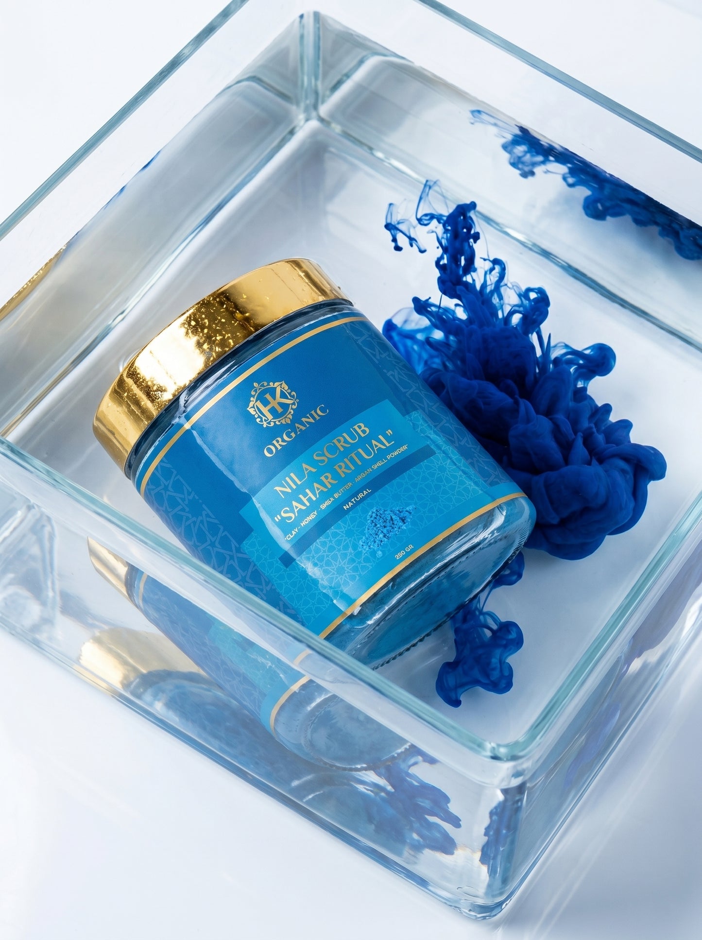 Blue skincare jar with gold cap in a clear box on a white background
