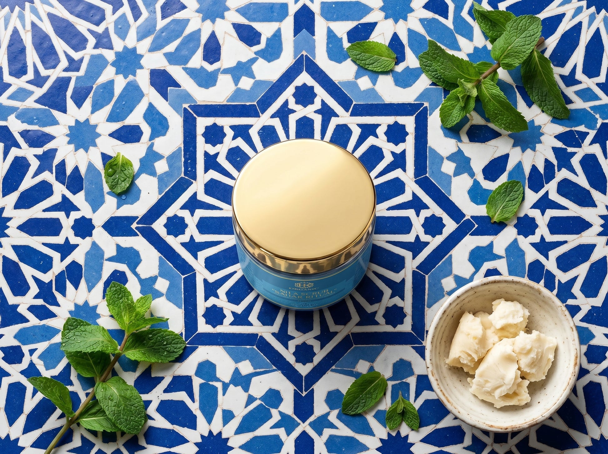 Blue jar with gold lid on a blue patterned tile background with mint leaves