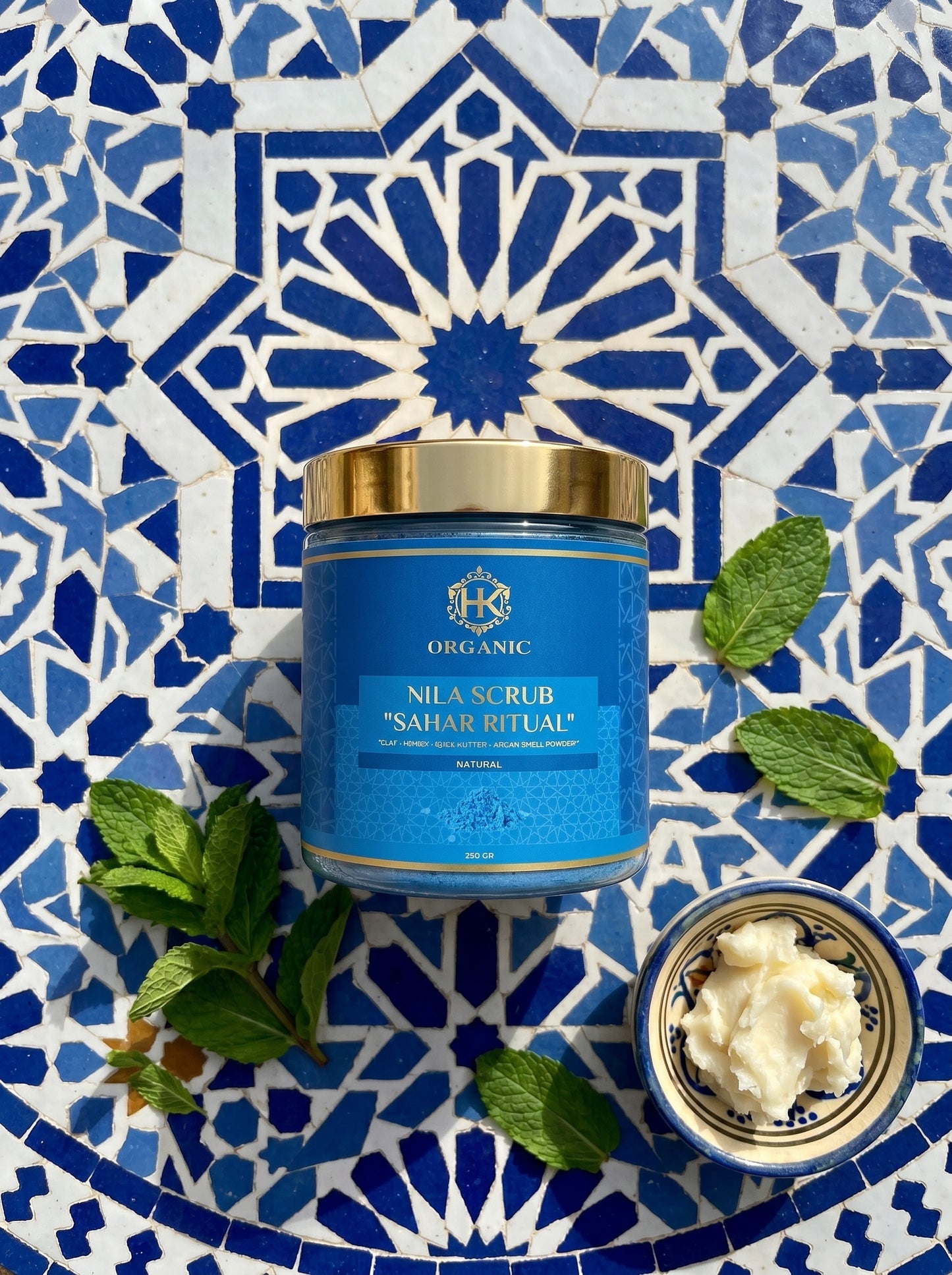 Blue scrub container with gold lid on a blue and white mosaic background
