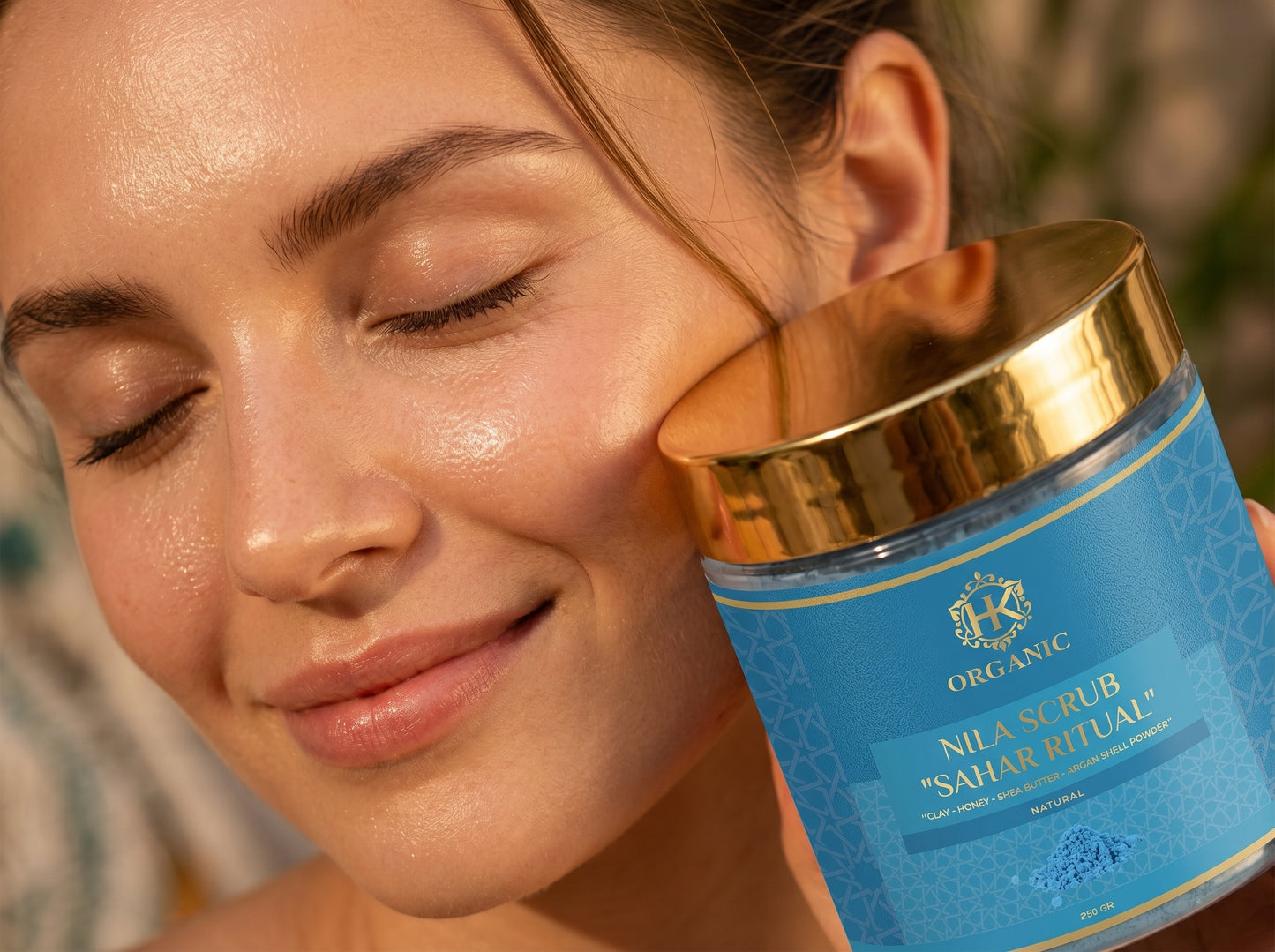 Woman applying a blue scrub to her face with a jar labeled 'Nila Scrub Sahar Ritual' in the foreground.