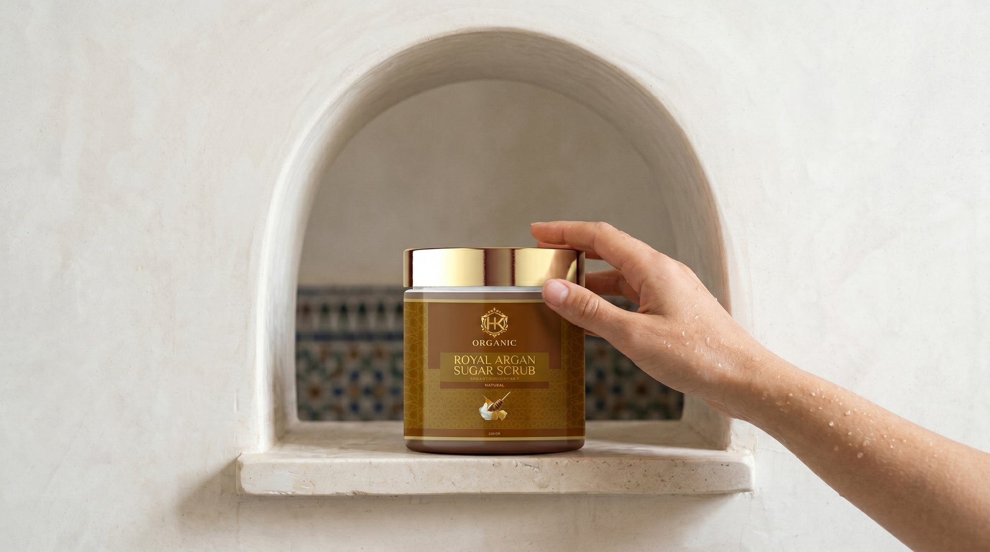 Hand holding a jar of organic cream scrub on a white shelf with a decorative background