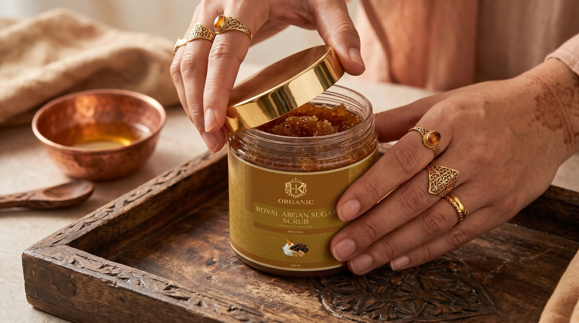 Person opening a jar of Royal Argan Seed Oil on a wooden tray with a bowl and spoon.