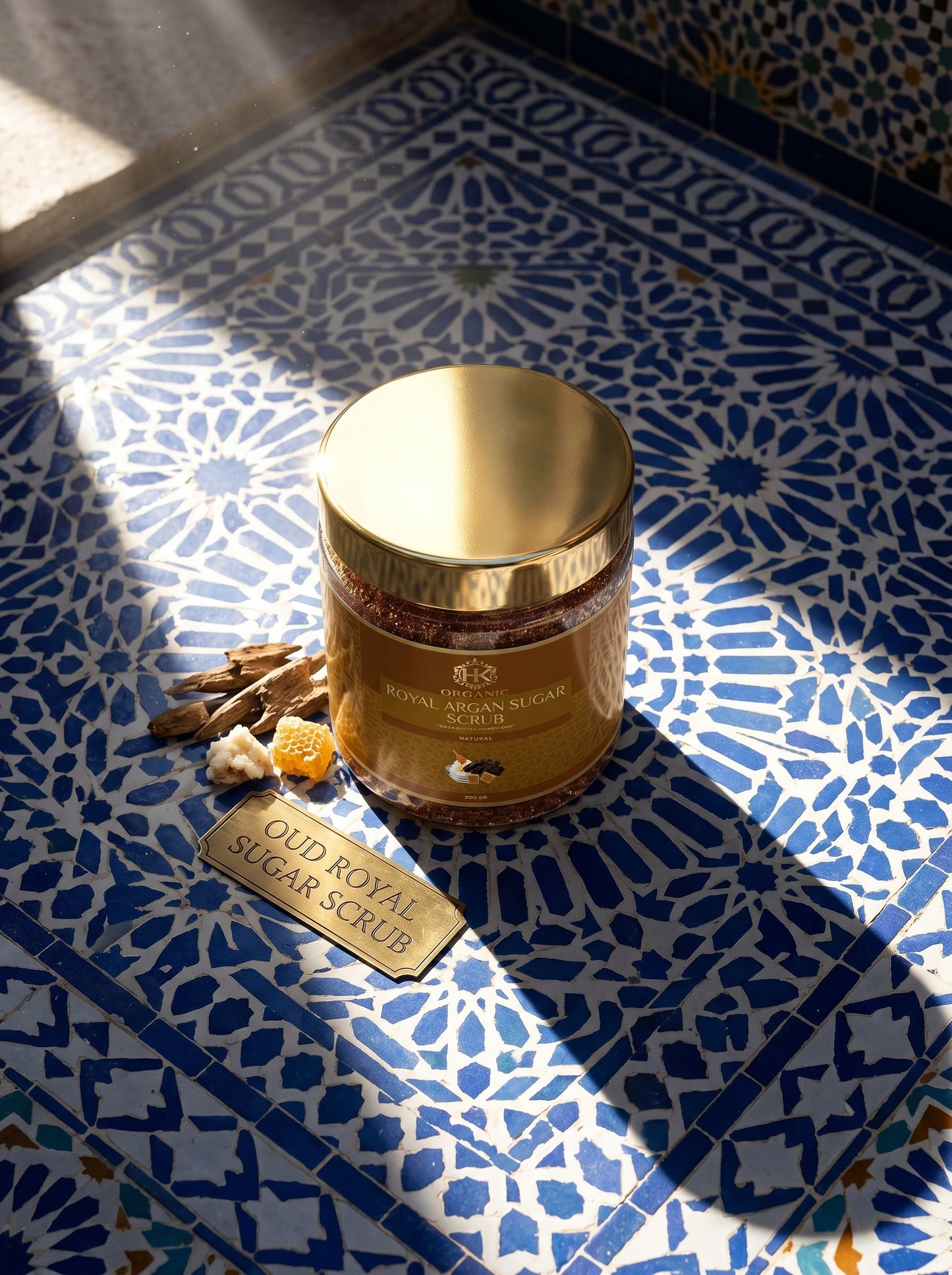 Gold jar of Oud Royal Sugar Scrub on a blue and white patterned tile floor