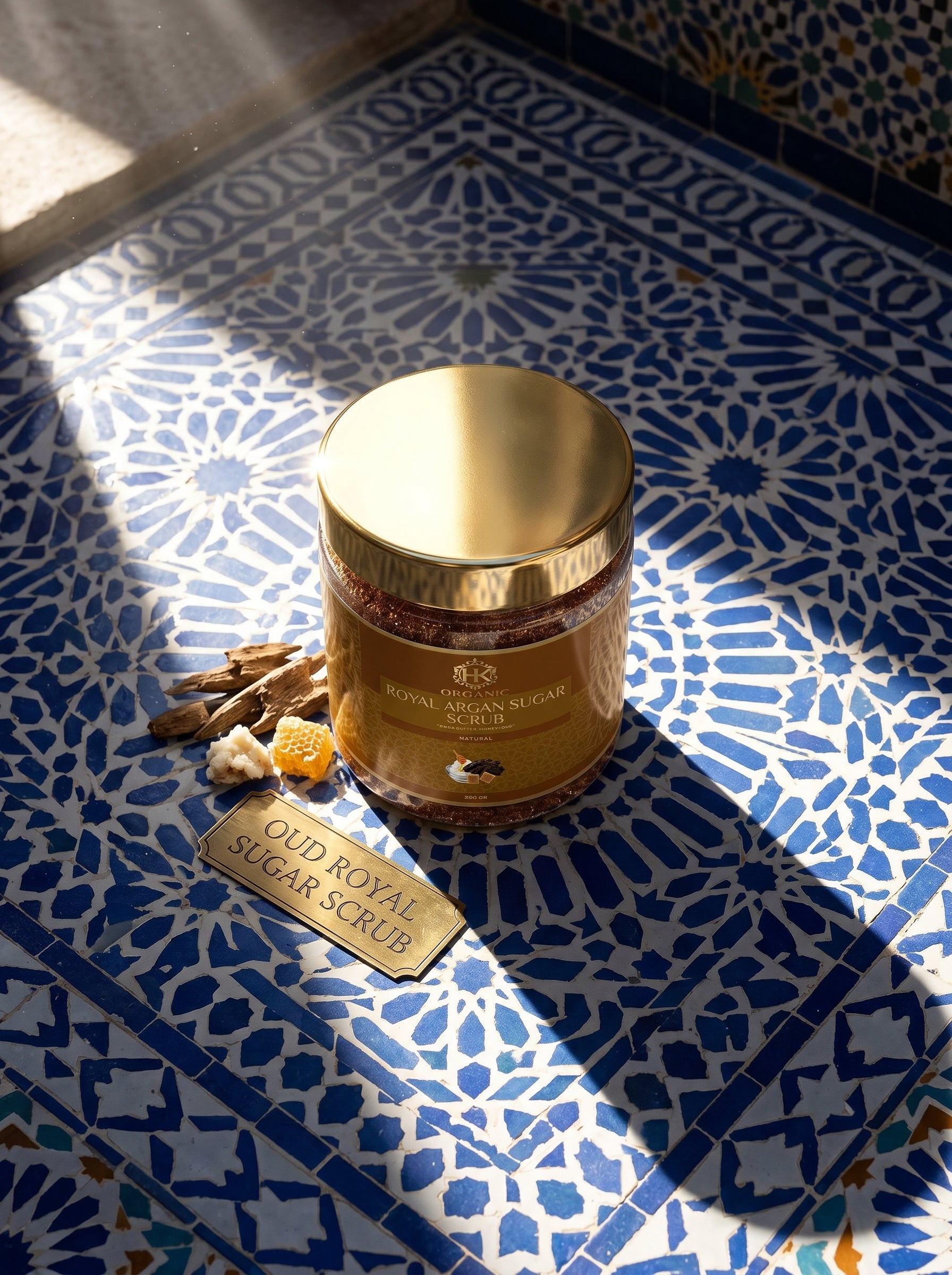 Gold jar of Oud Royal Sugar Scrub on a blue and white patterned tile floor