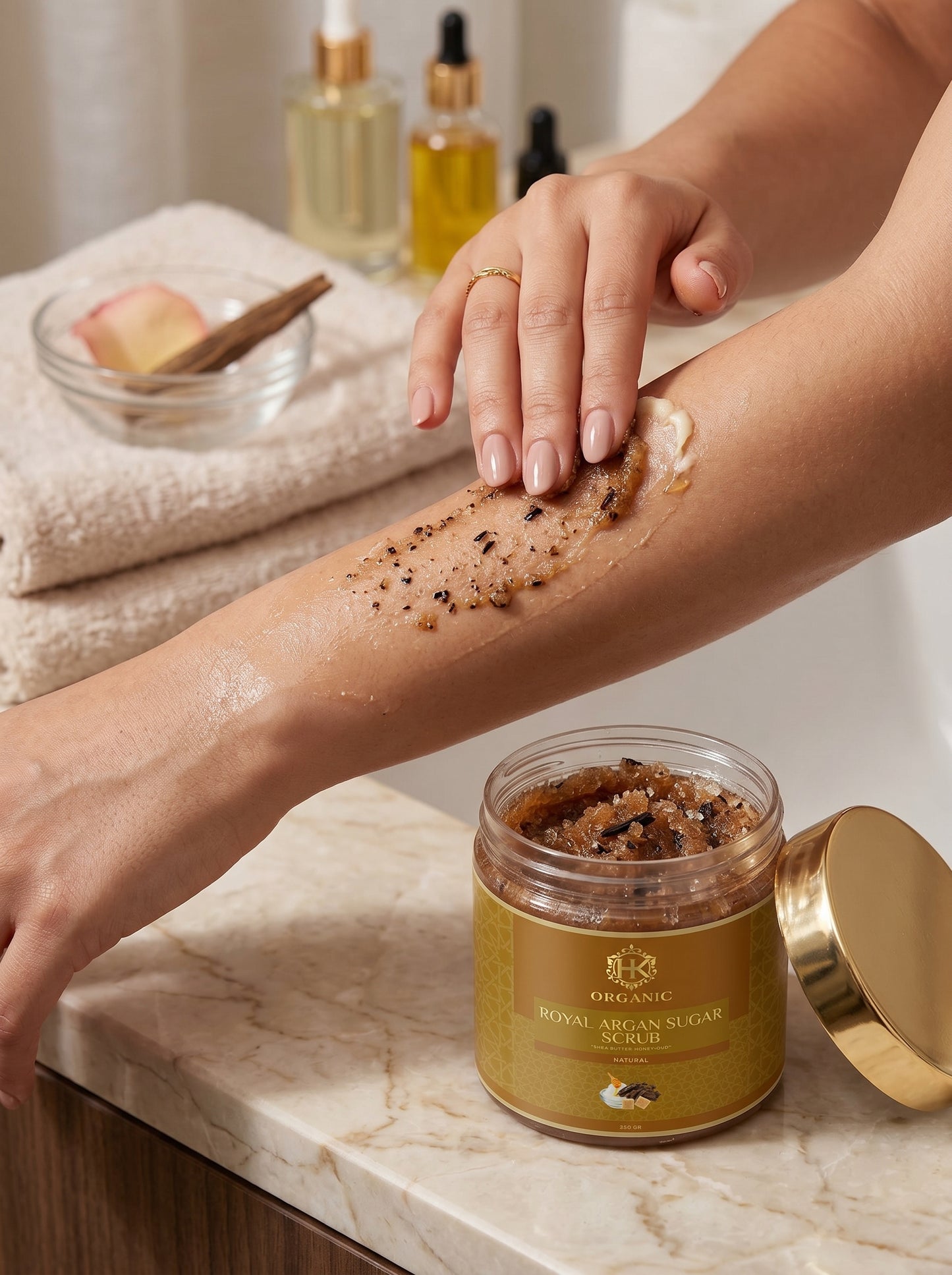 Person applying a scrub to their arm with a jar of scrub and skincare products in the background.