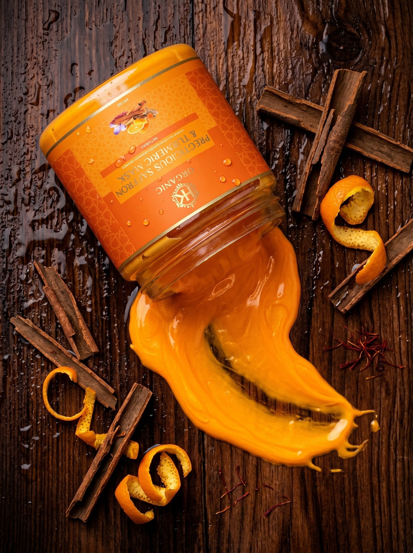 Jar of turmeric with a stream of turmeric flowing out, surrounded by cinnamon sticks and orange peels on a wooden surface.