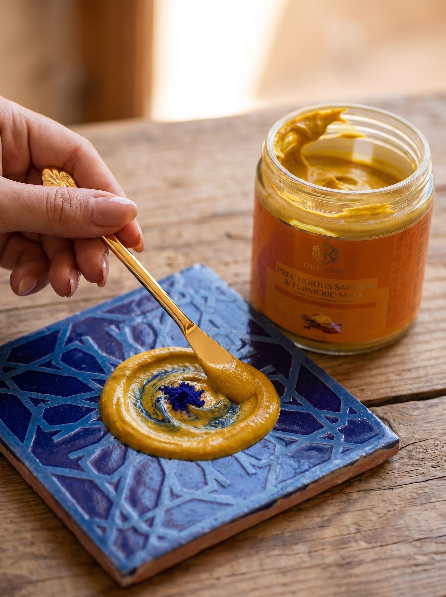 Jar of turmeric  with a spoon on a blue textured coaster, on a wooden surface.