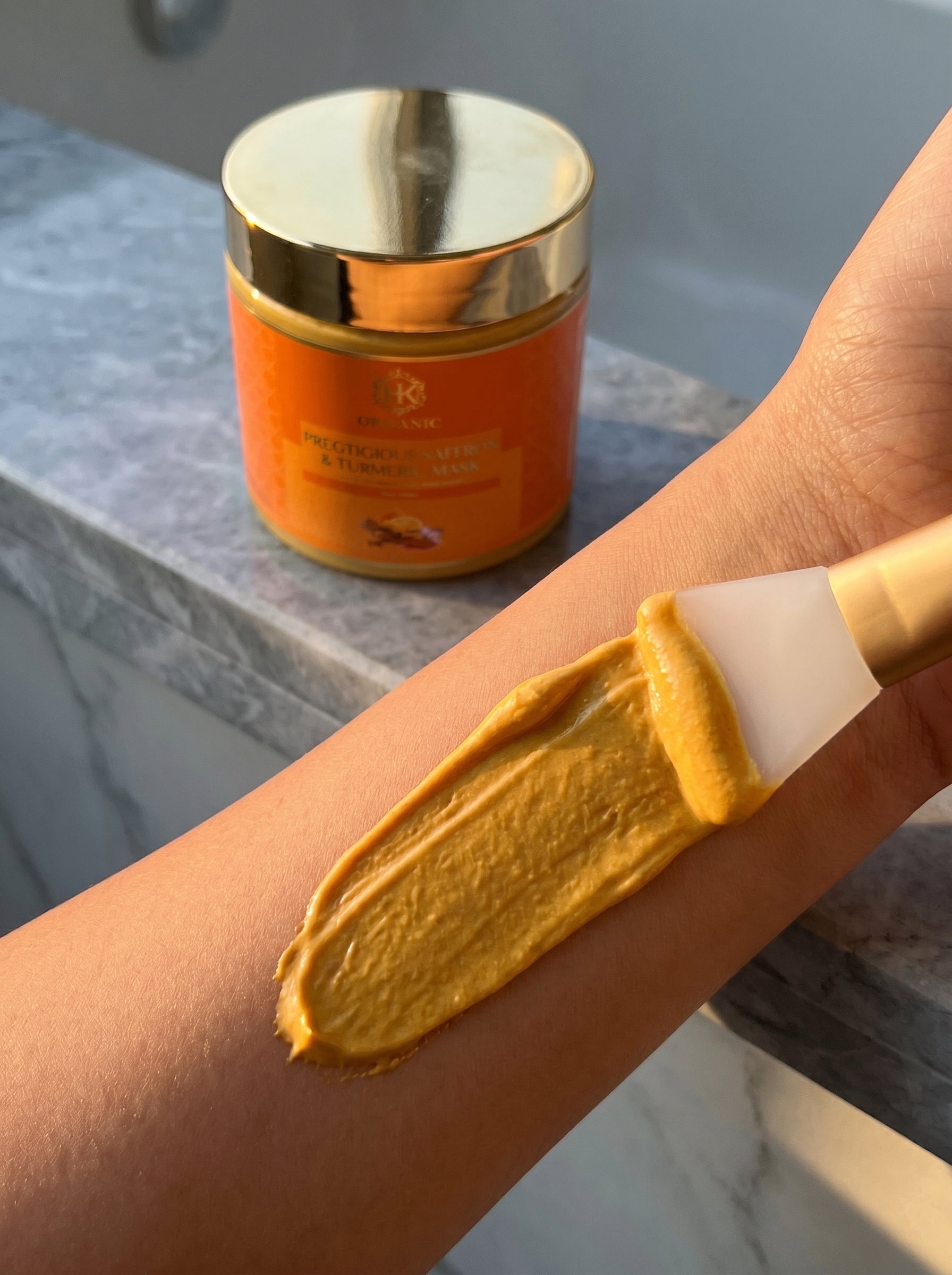 turmeric cream being applied to a person's arm with a gold and white container in the background.