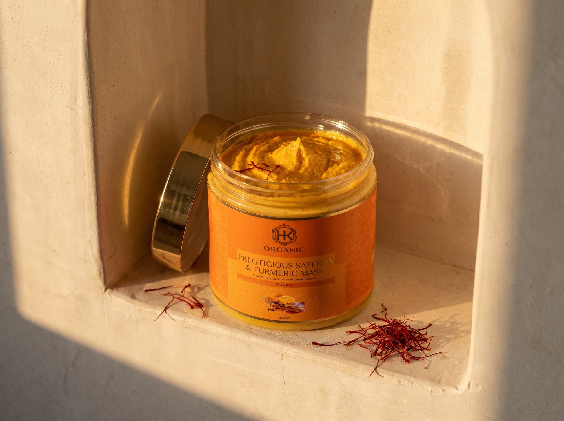 Jar of organic saffron and turmeric mask on a textured surface with saffron strands.