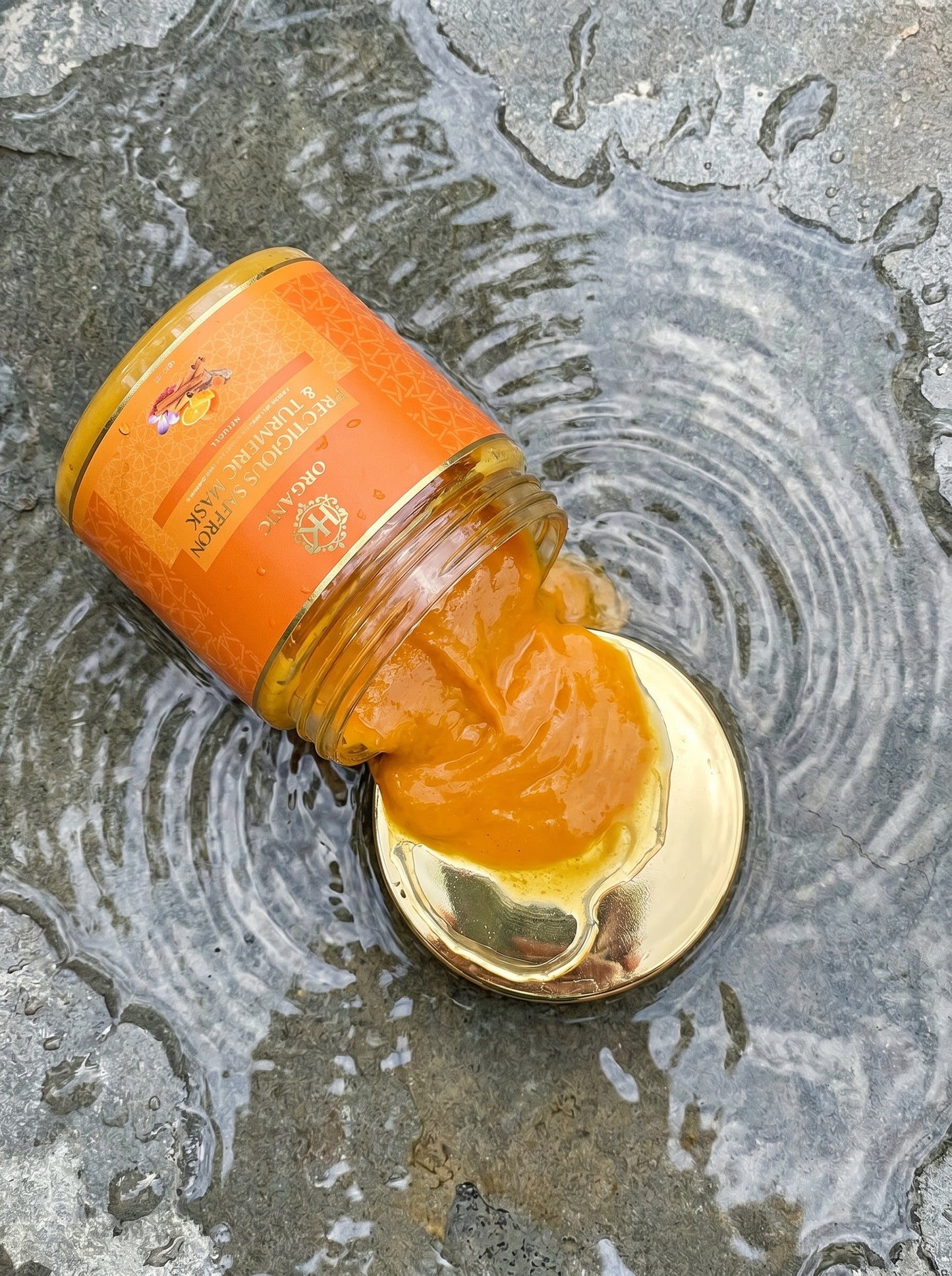 Open jar of turmeric spread with a gold lid on a wet surface