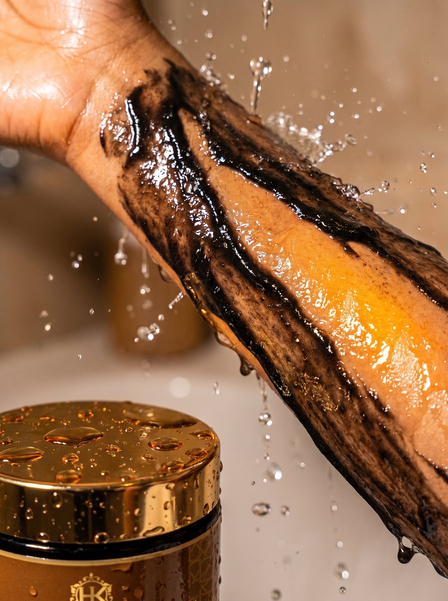 Hand with black hair removal cream applying cream to leg, with a gold container in the foreground.