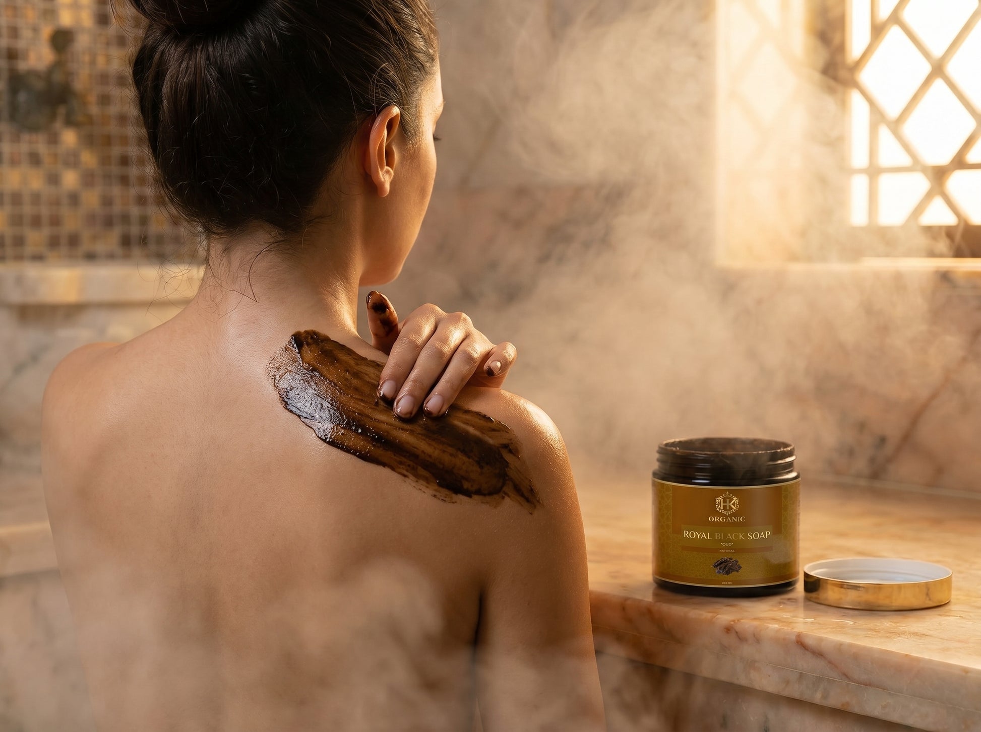 Person applying a scrub to their shoulder with a jar of scrub on a marble surface.