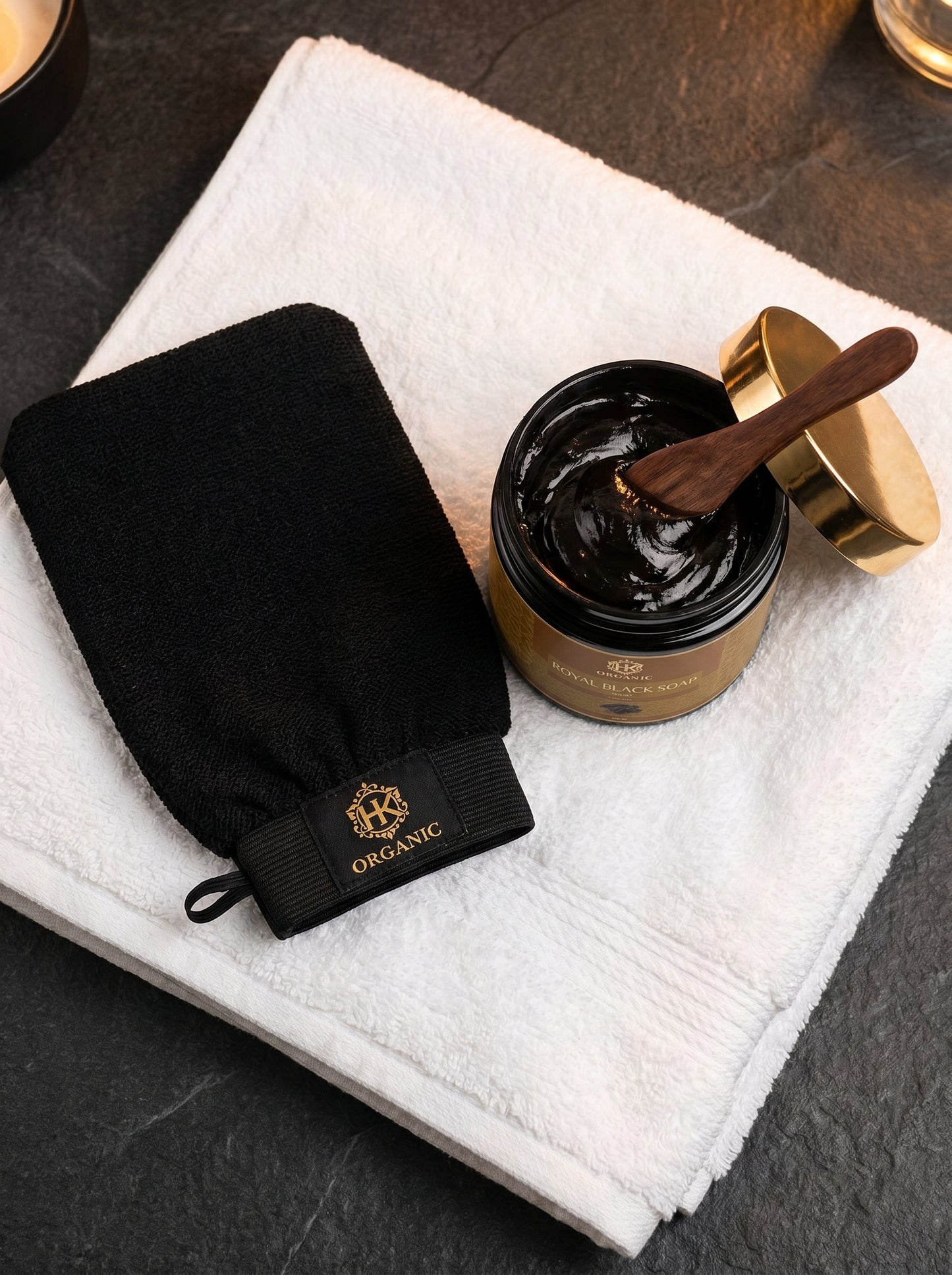 Black glove and jar of black cream on a white towel with a wooden spoon.