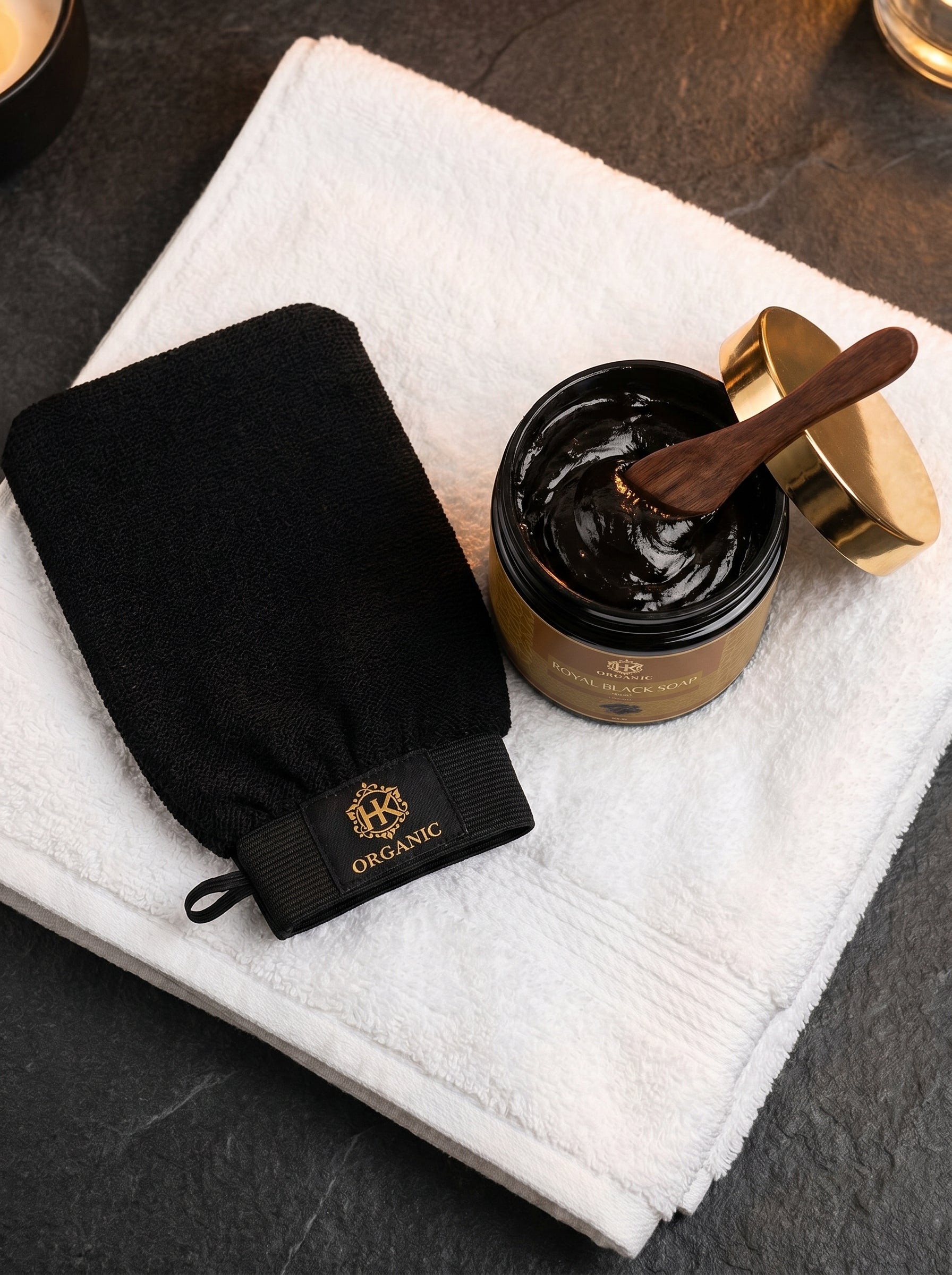 Black glove and jar of black cream on a white towel with a wooden spoon.