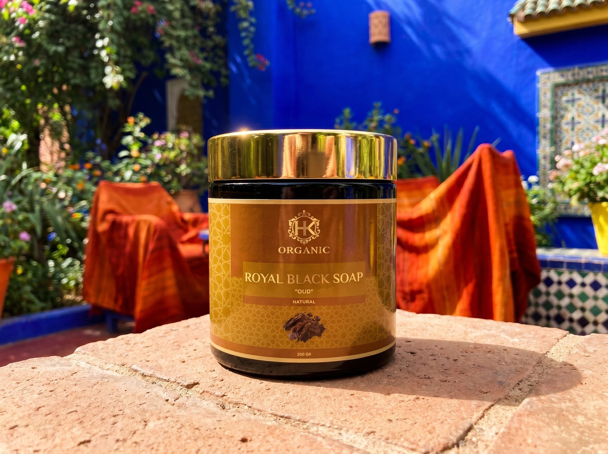 Container of Organic Royal Black Soap on a stone surface with a colorful outdoor background