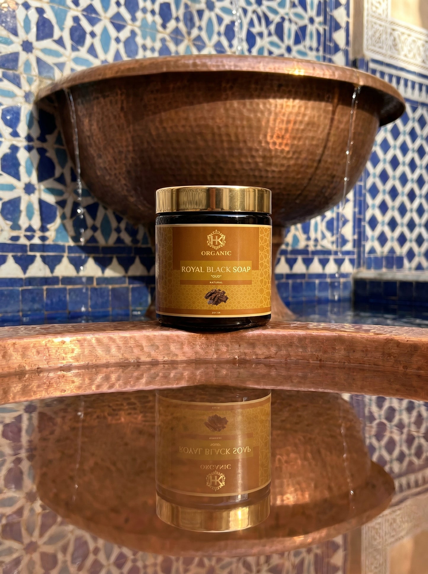 Jar of Royal Black Soap on a reflective surface with a decorative blue and white tiled wall in the background.