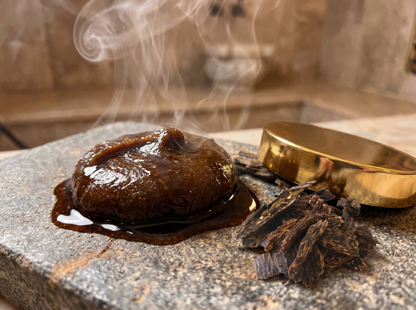 Smoking chocolate truffle on a stone surface with a gold container in the background.