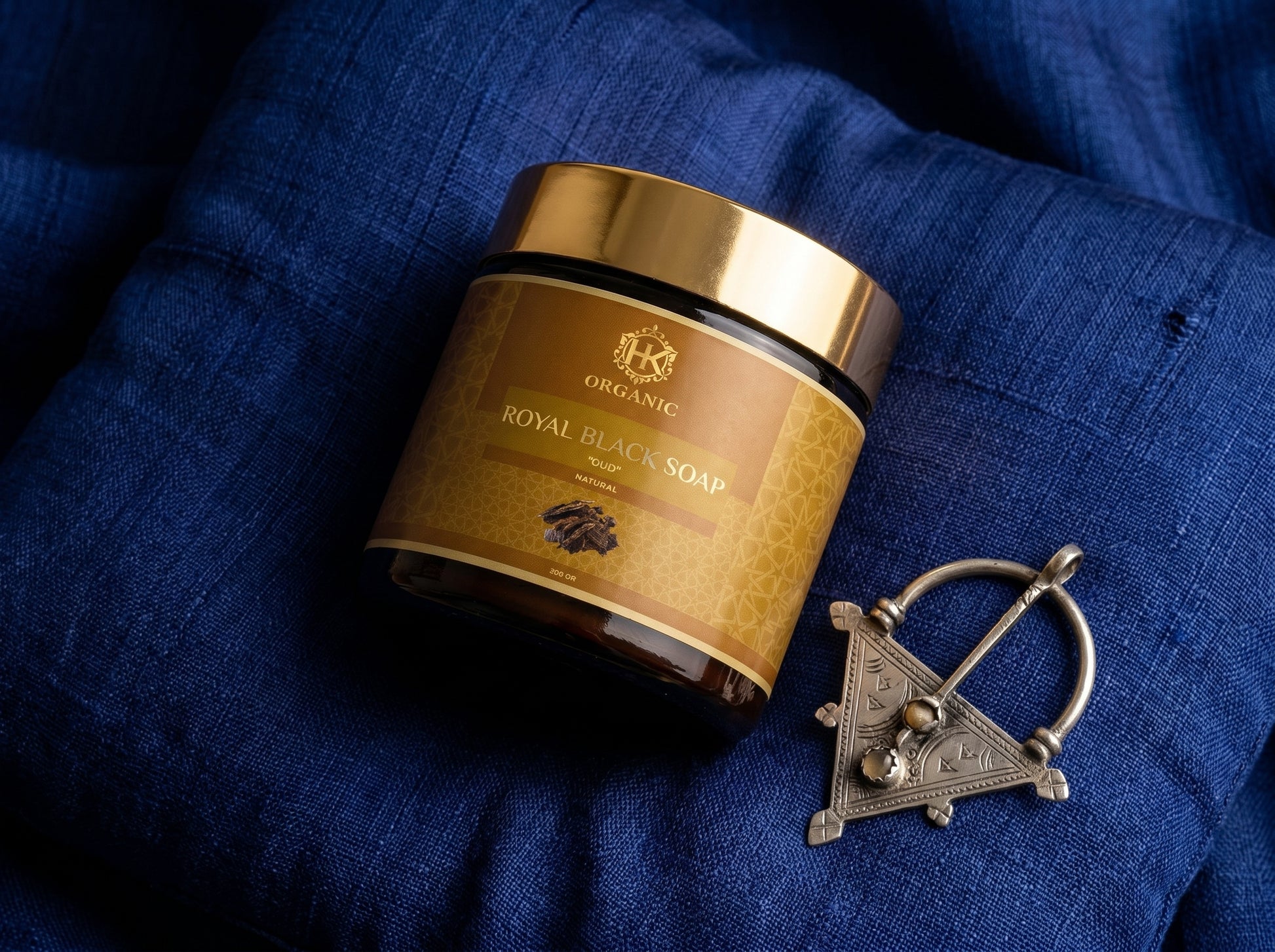 Jar of Royal Black Soap on a blue fabric background with a decorative brooch.