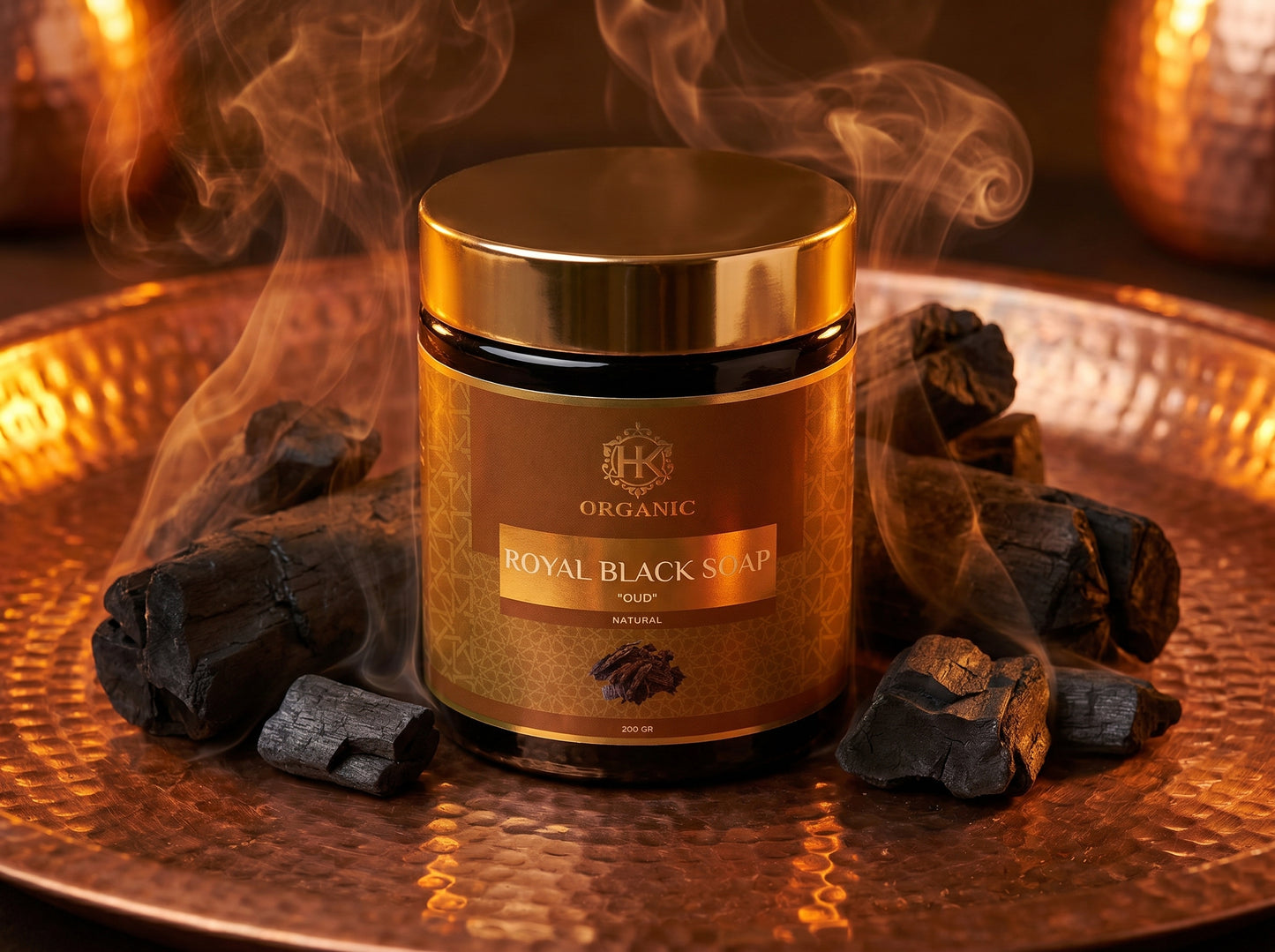 Gold jar of organic royal black soap on a reflective surface with smoke and charcoal.