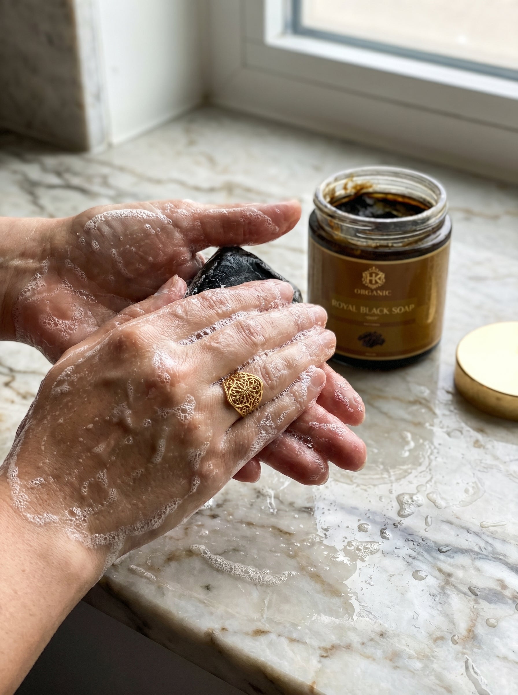 Person applying soap to hands with a jar of soap in the background on a marble surface.