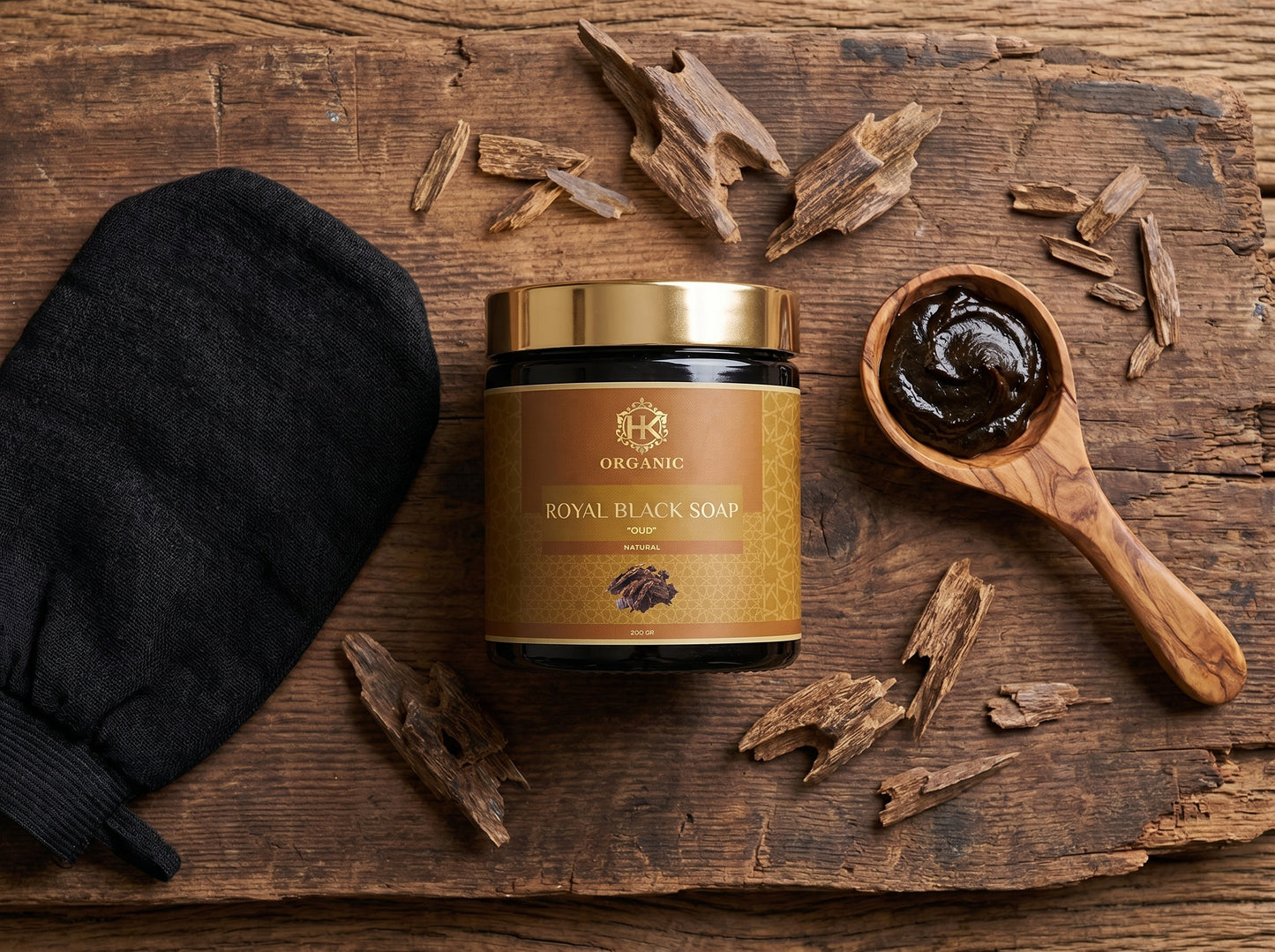 Jar of organic royal black soap with a wooden spoon filled with soap, on a rustic wooden surface.