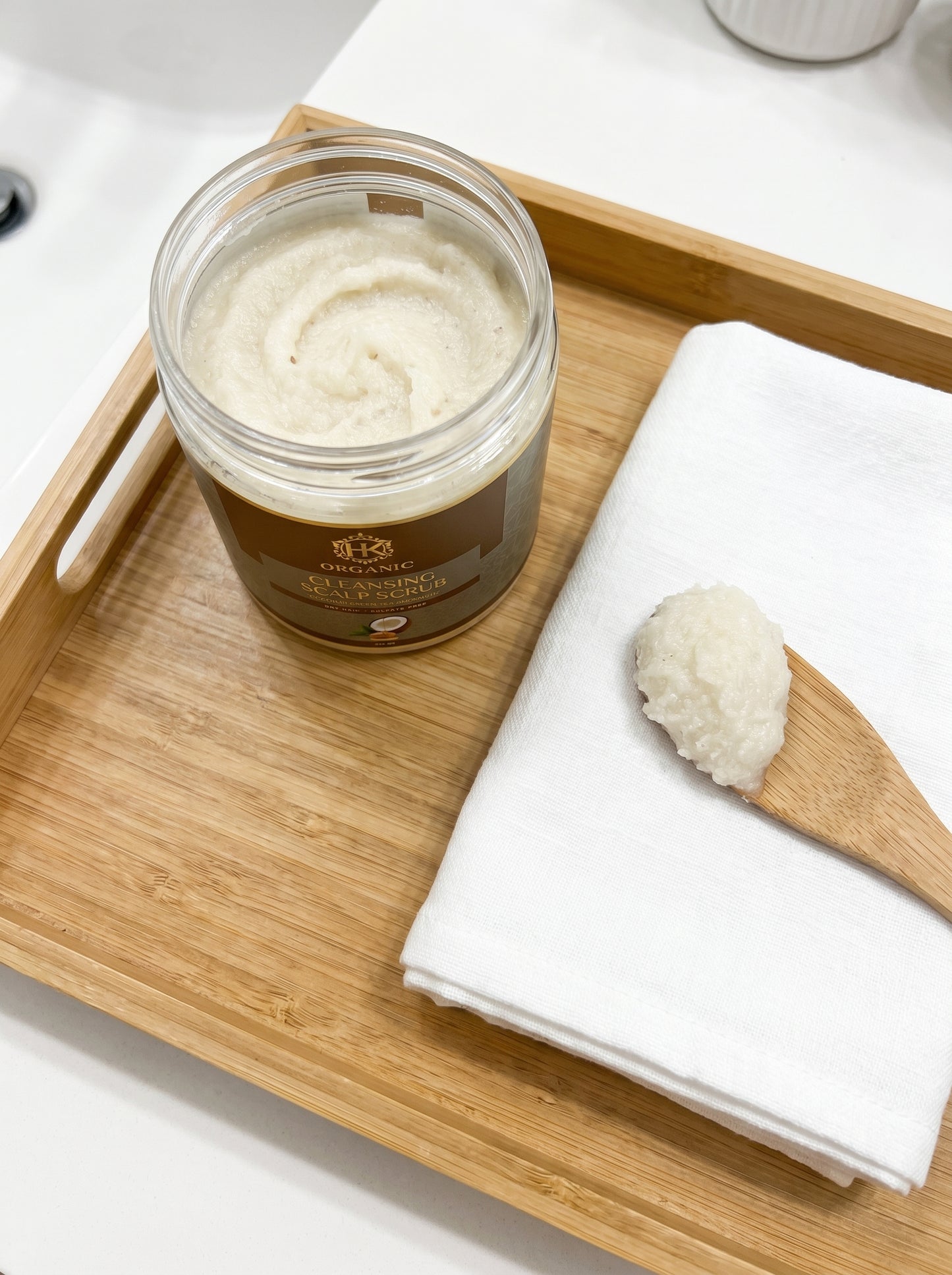 Jar of white cream on a wooden tray with a wooden spoon and white cloth.