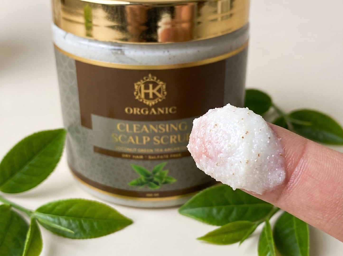 Cleansing scalp scrub with a container labeled 'HK Organic' on a white background with green leaves.