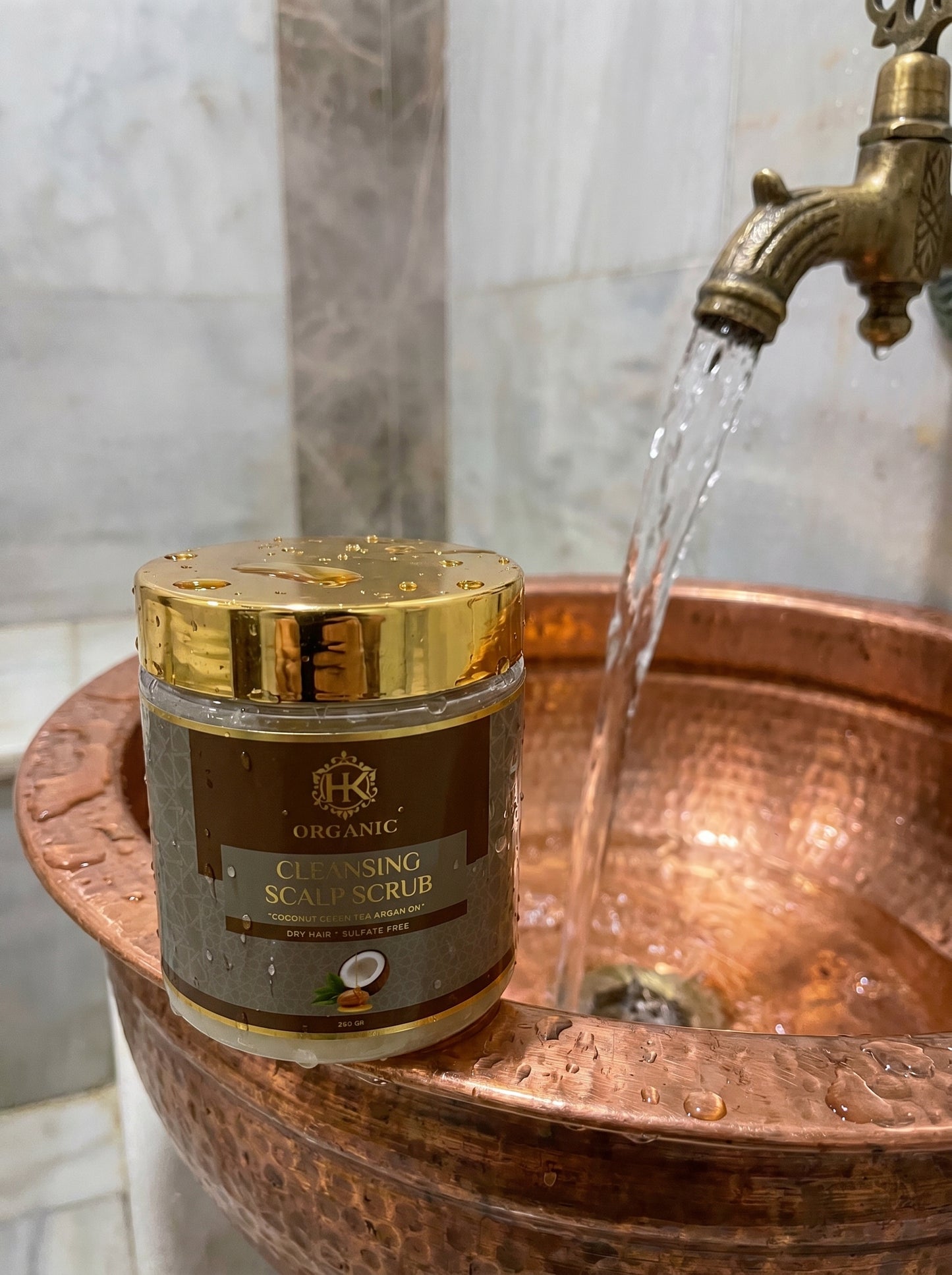 Jar of organic cleansing scalp scrub on a copper sink with water flowing.