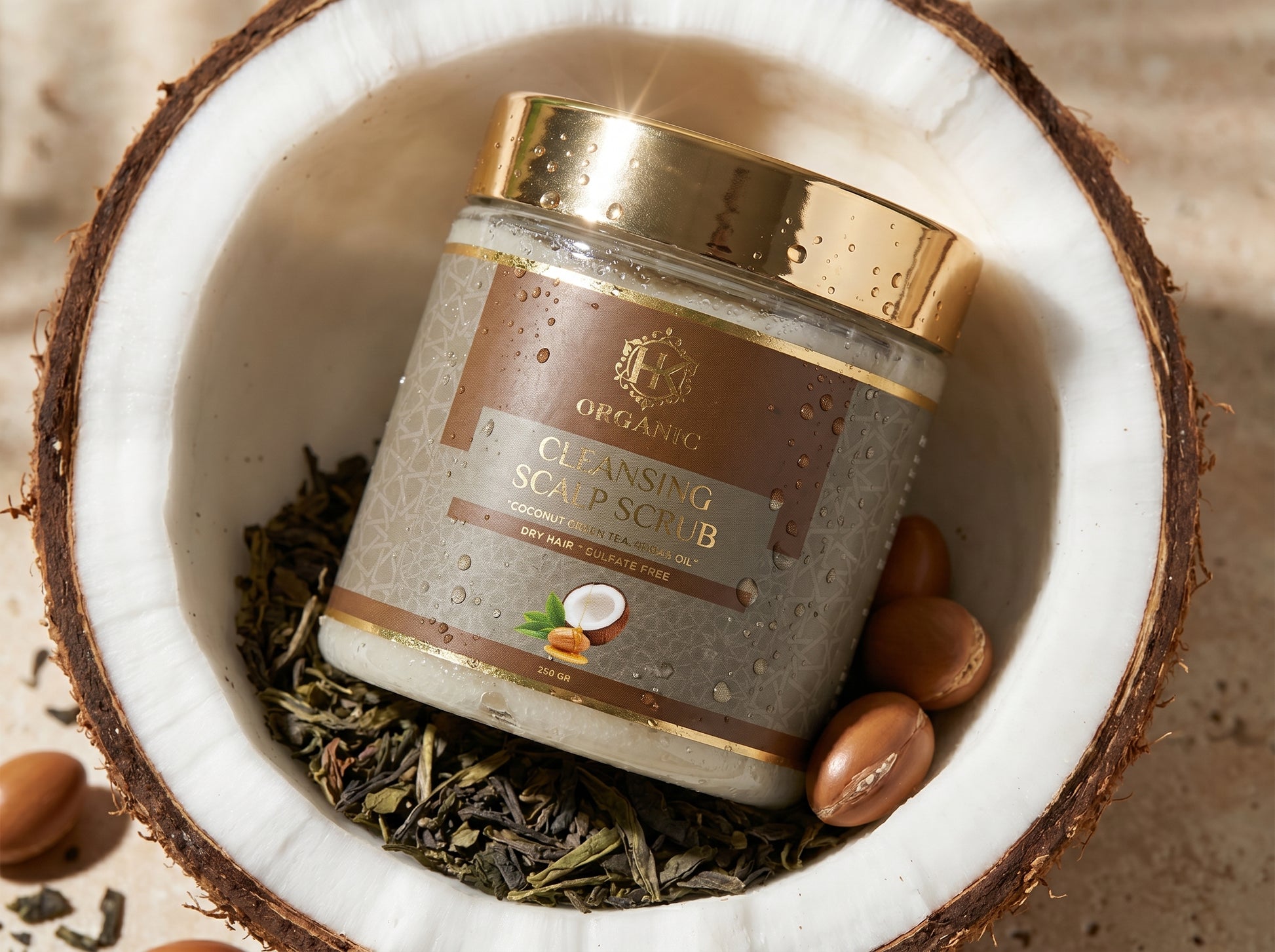 Jar of cleansing soap scrub with a gold lid inside a coconut shell with herbs and nuts.