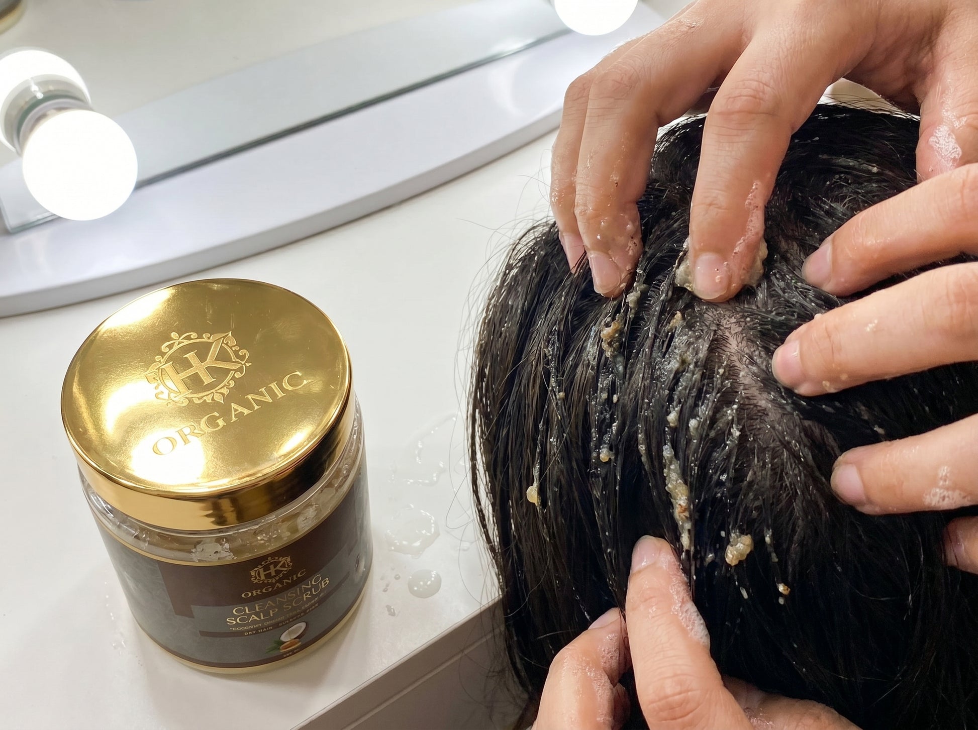 Person applying a hair product to their hair with a jar of hair product next to them.