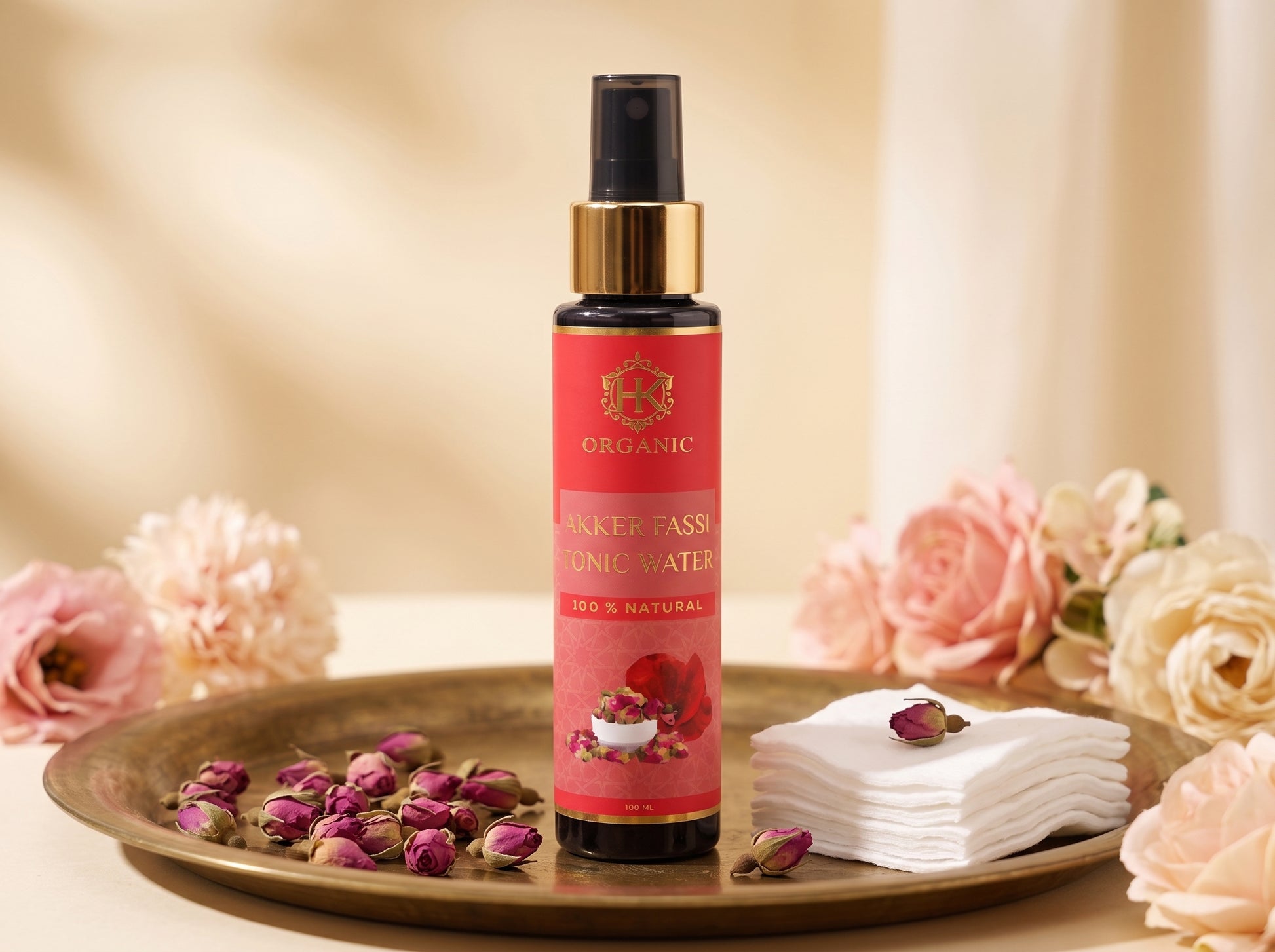 A bottle of Organic Alkaline Passivated Organic Water (OPW) with a pink label and gold collar, displayed on a gold tray with dried rose petals, white cotton pads, and pink roses against a warm beige background.