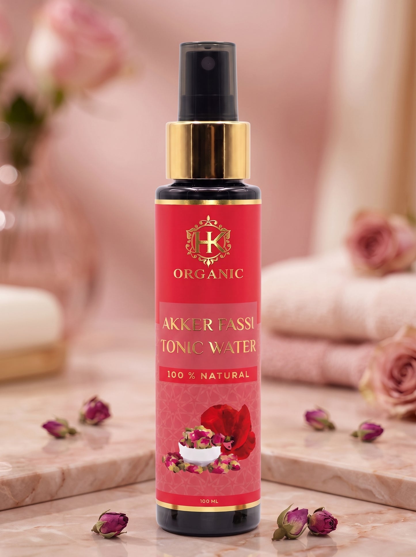 A bottle of Akker Passi Organic Aromatic Tonic Water with a red label and gold pump, set on a marble surface with pink roses and folded towels in the background.