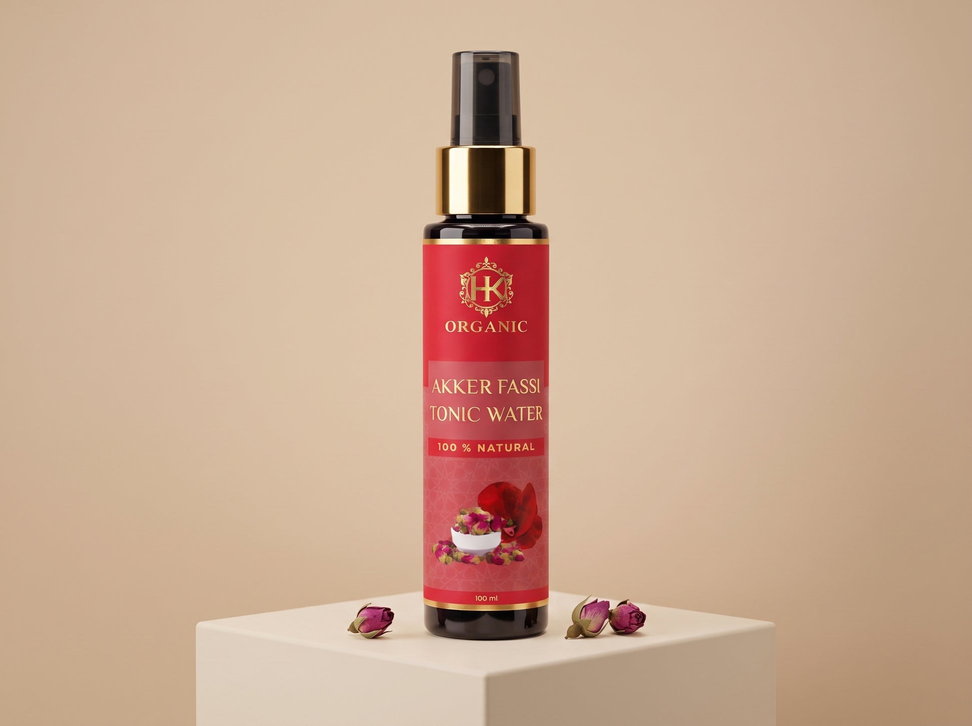 A bottle of Organic Akker Fassi Tonic Water with a red label and gold collar, displayed on a white pedestal with dried rose petals against a beige background.