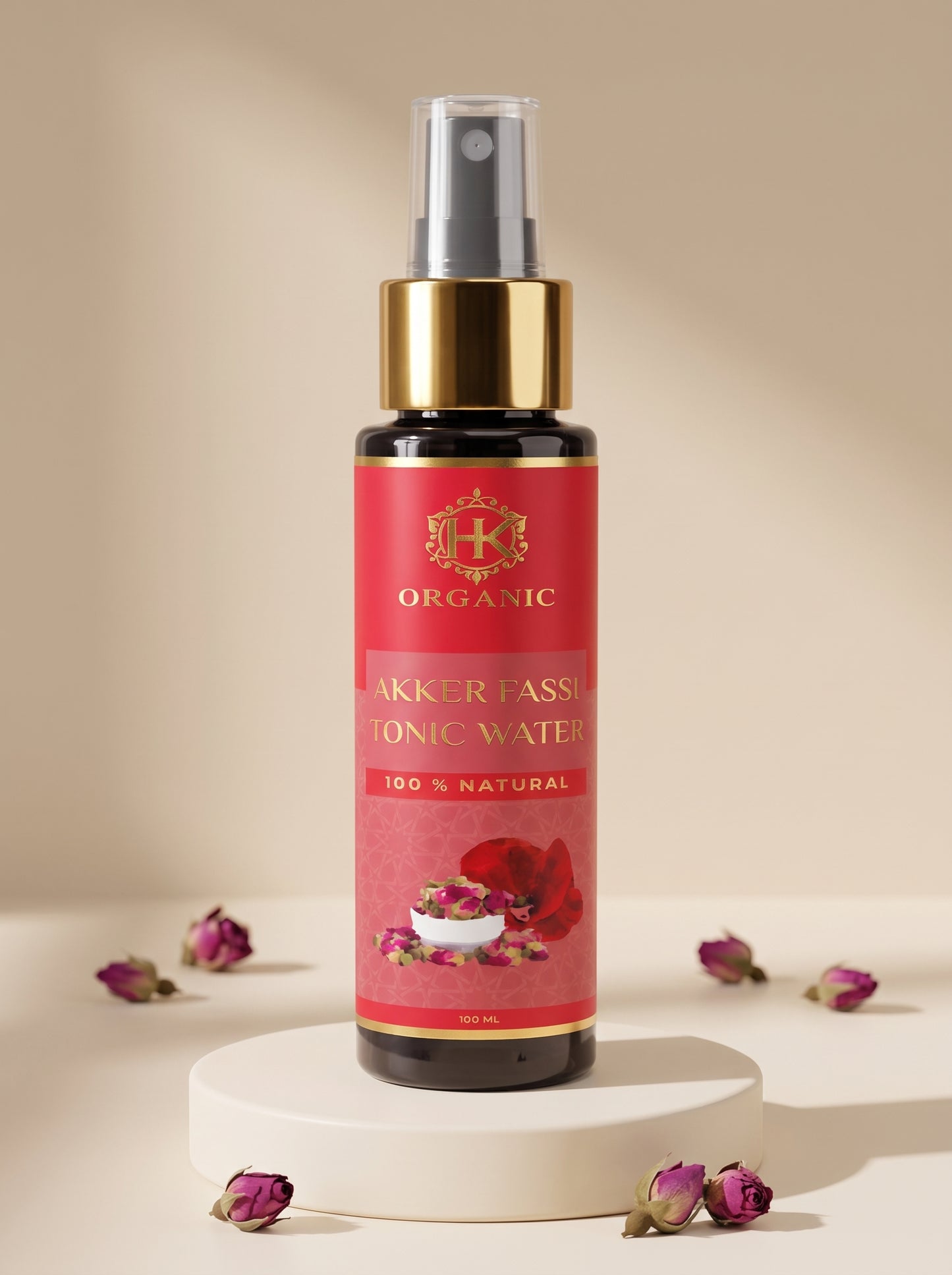 A bottle of Akker Fassa Organic Akker Fassa Ionic Water spray with a red label and gold pump, displayed on a white pedestal with scattered rose petals against a beige background.