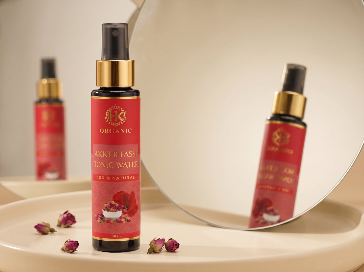 A bottle of Organic Akker Fasi Tonic Water with a red label and gold collar, displayed on a beige platform with a mirror reflecting its image in the background.