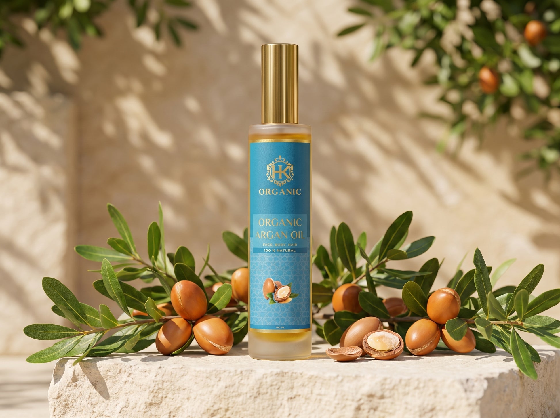 A bottle of Organic Argan Oil stands on a stone surface surrounded by argan branches and nuts, with a warm beige wall and leaf shadows in the background.