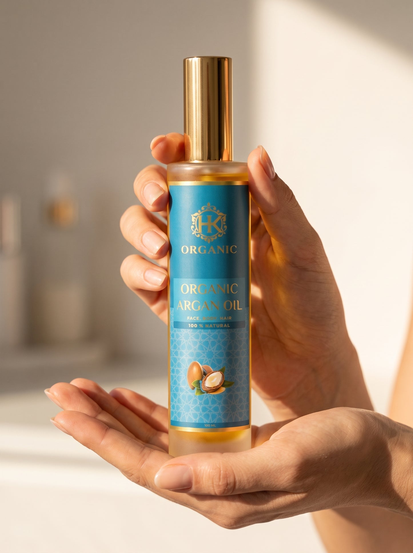 A hand holding a bottle of HK Organic Organic Argan Oil against a softly blurred warm-toned background.