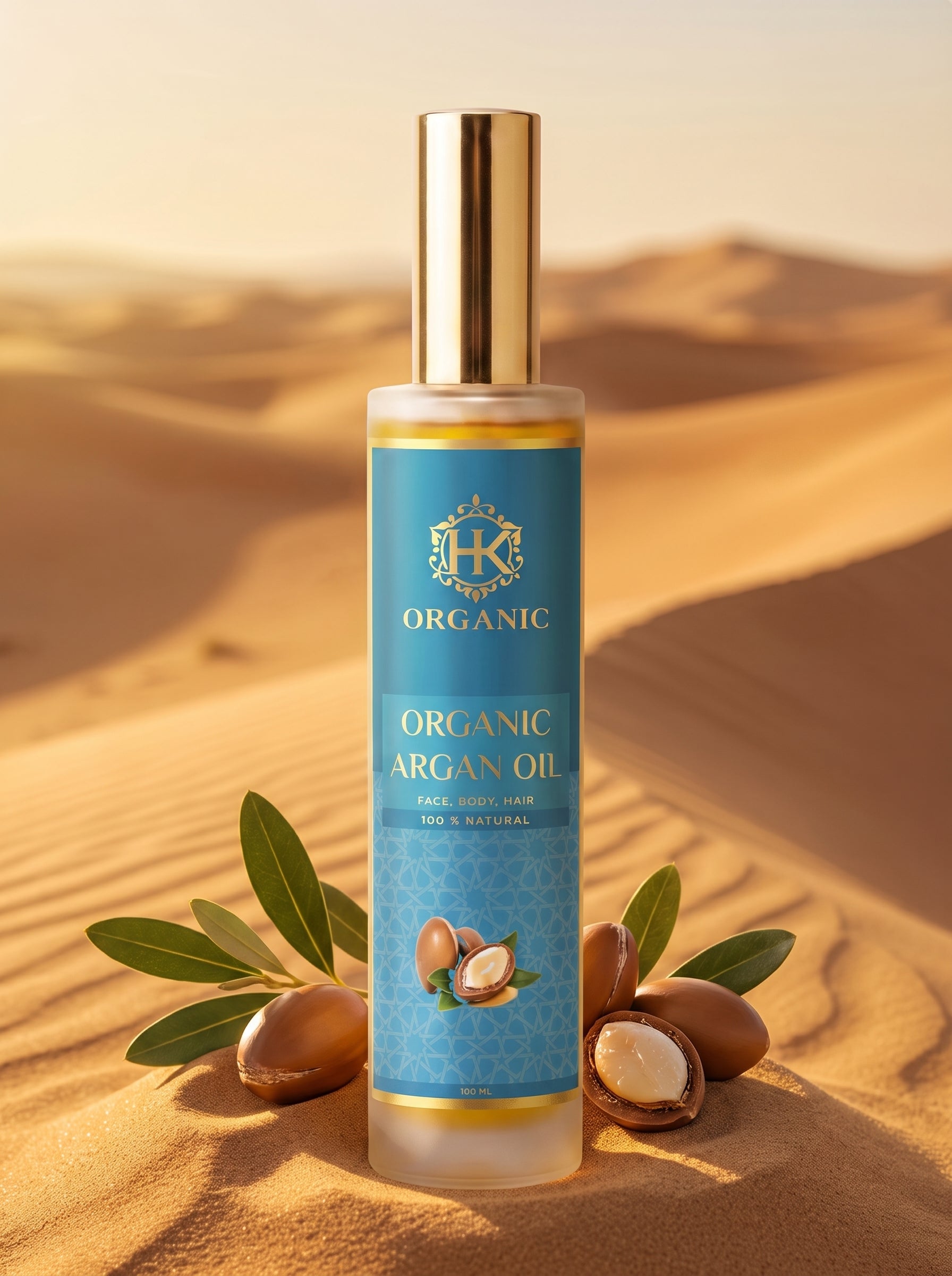 A bottle of Organic Argan Oil stands on sand in a desert landscape, with argan nuts, green leaves, and a gold cap visible. The product label is blue with gold lettering and a crest logo.