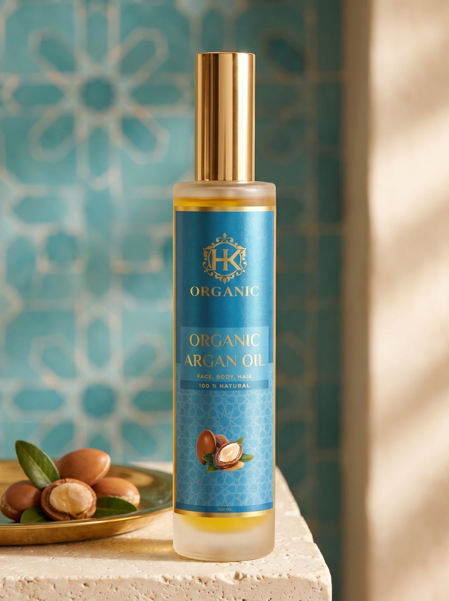 A bottle of HK Organic Argan Oil stands on a stone surface with argan nuts and leaves beside it, set against a turquoise patterned tile background with warm light on the right.