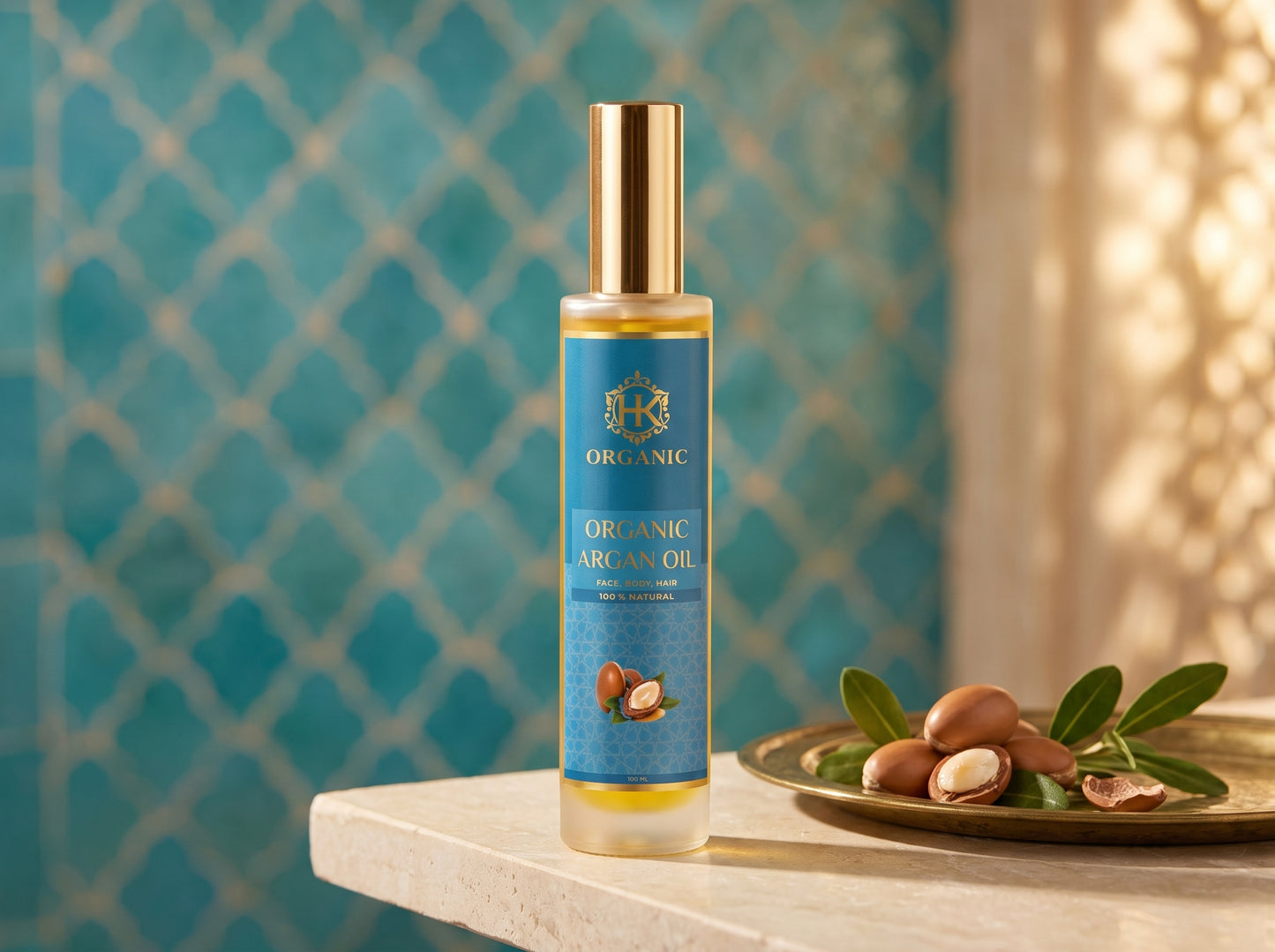 A bottle of Organic Argan Oil stands on a light stone surface next to a plate of argan nuts and green leaves, with a turquoise patterned tile wall in the background.