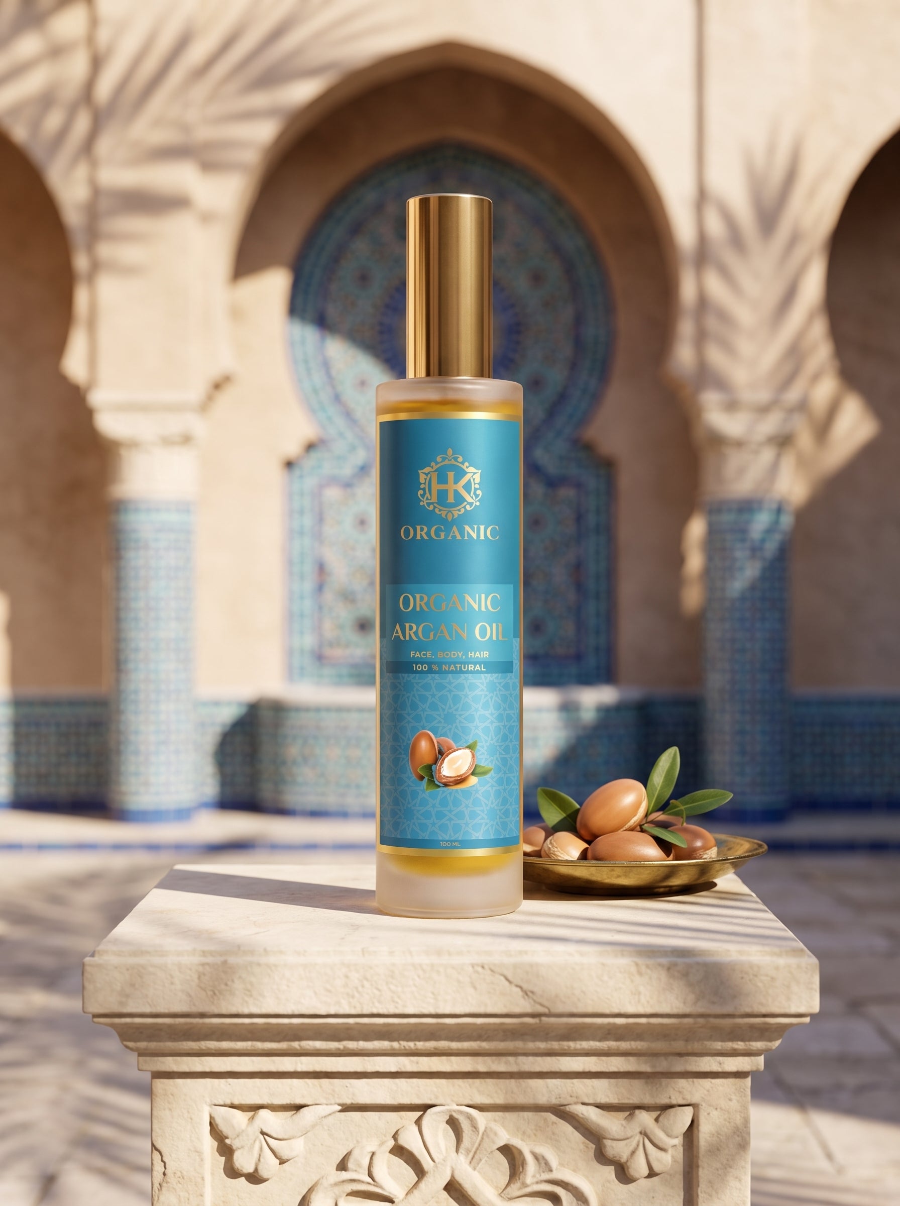 A bottle of Organic Argan Oil stands on a carved stone pedestal in front of a Moroccan-style archway with blue tile details. A small dish of argan nuts and green leaves sits beside the bottle.